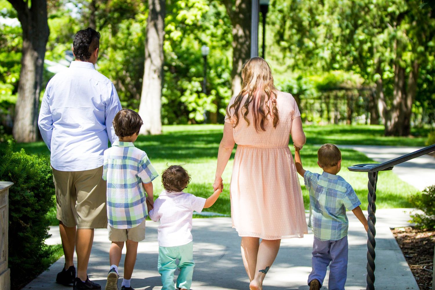 A family walking together on a tree-lined path during a sunny summer day.