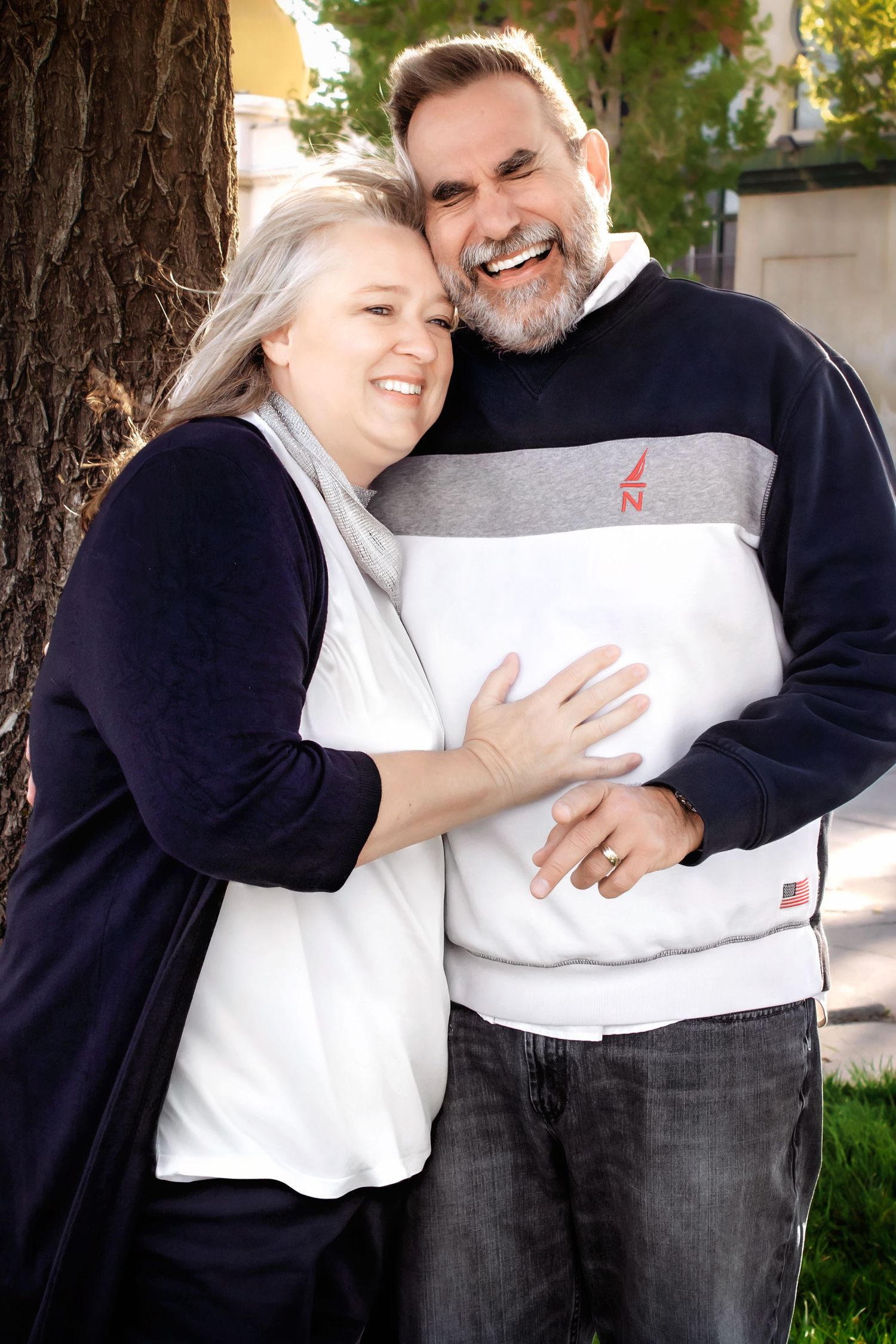 Couple embraces while standing near tree during outdoor portrait session.