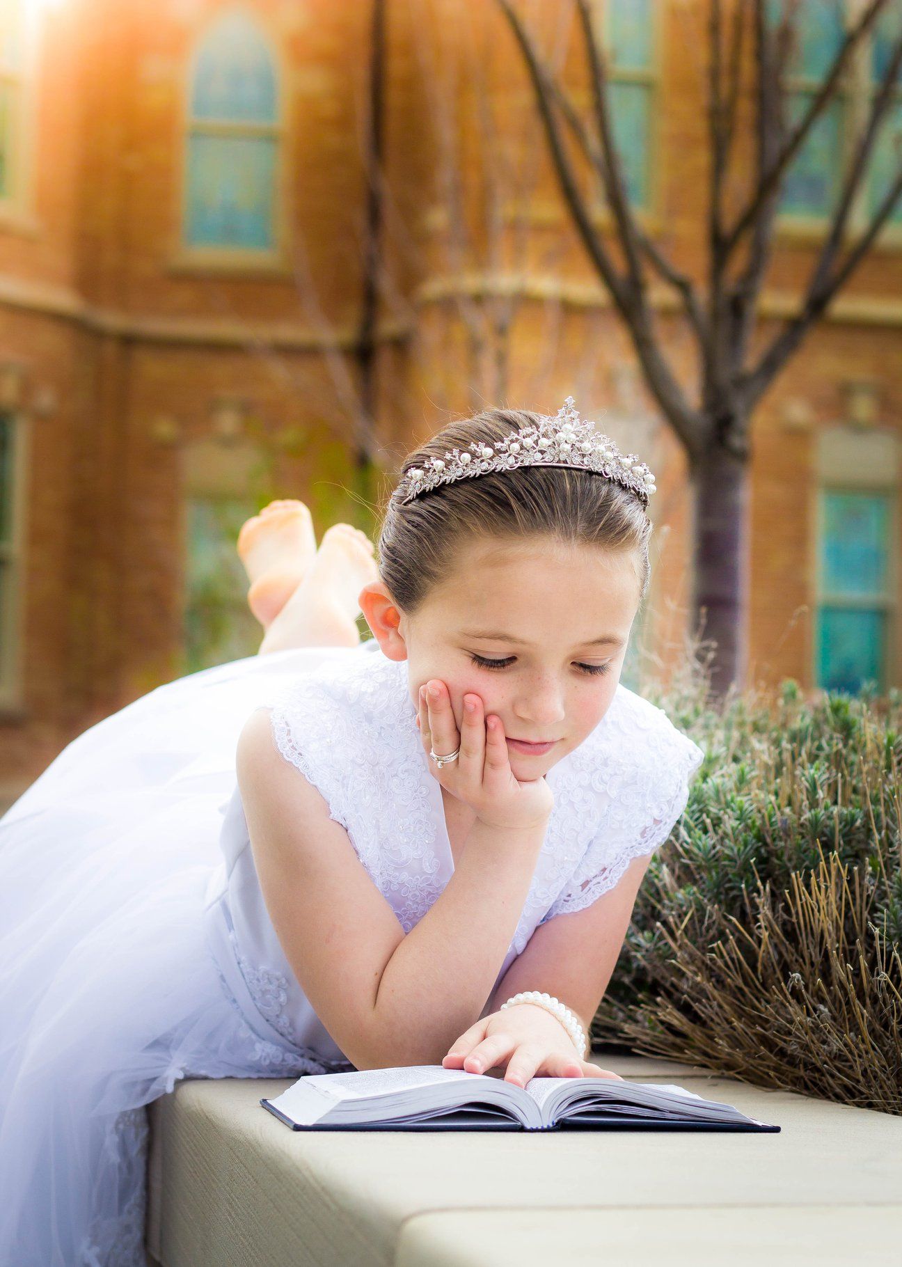 Person in white dress and tiara reading while lying on stone ledge outdoors.