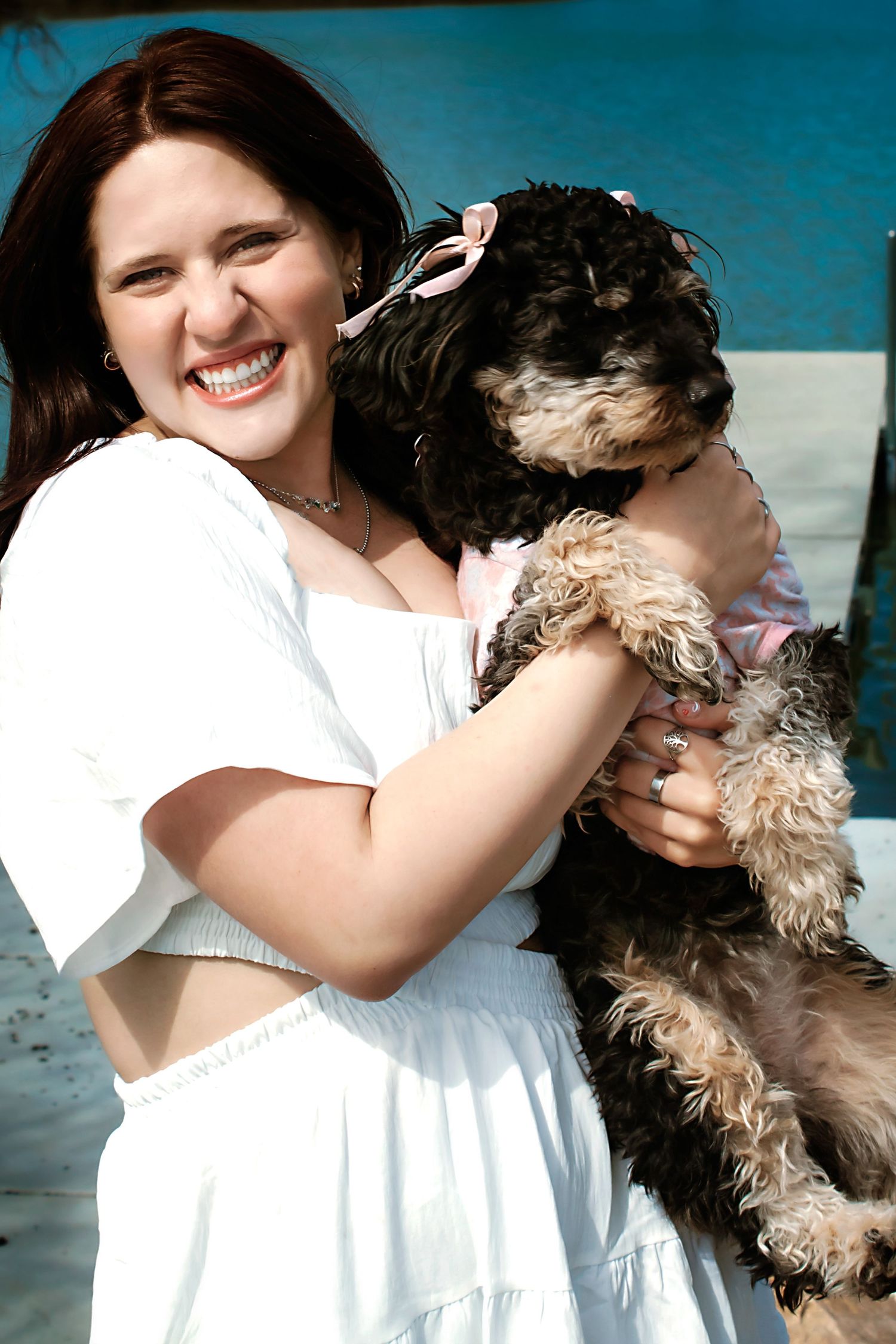 Person in white dress hugging fluffy black and white dog outdoors.