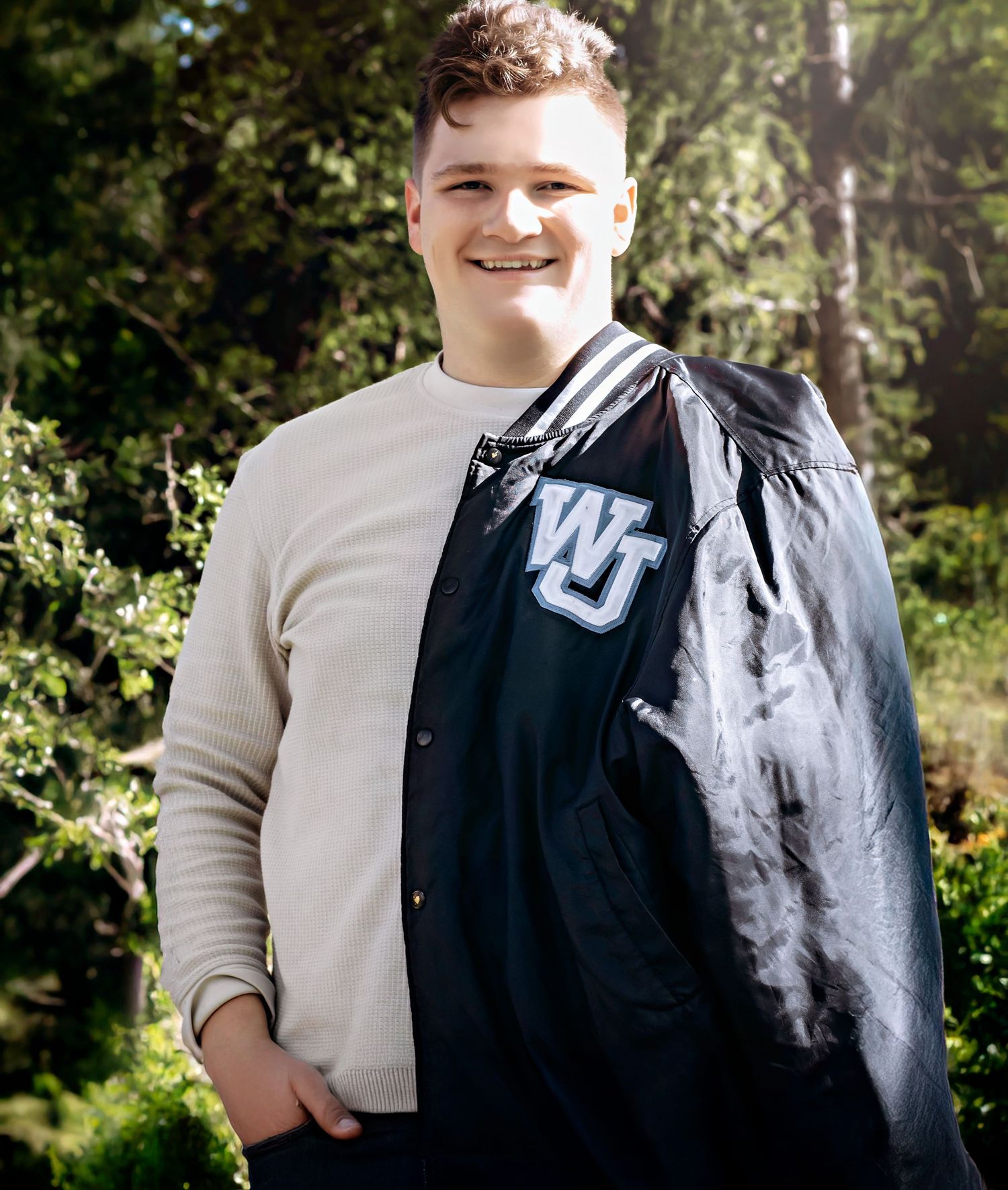 Student wearing cream sweater and black varsity jacket with WJ logo in outdoor setting.