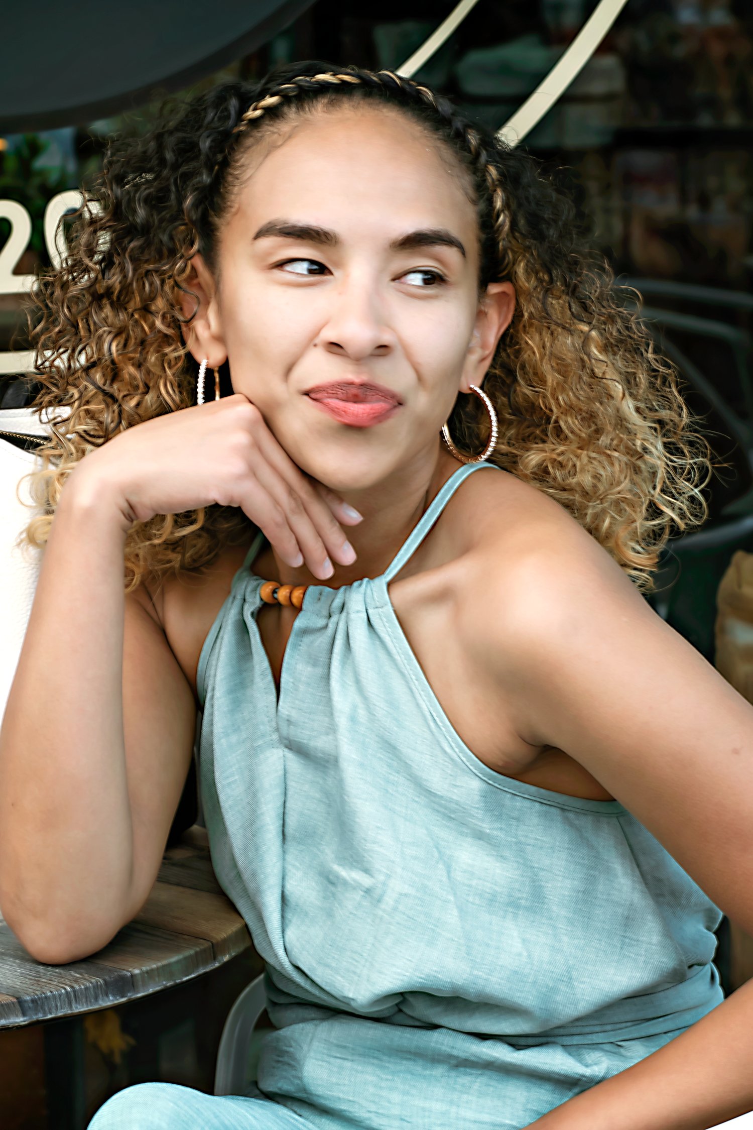 Person in mint green top poses playfully with curly hair and hoop earrings.
