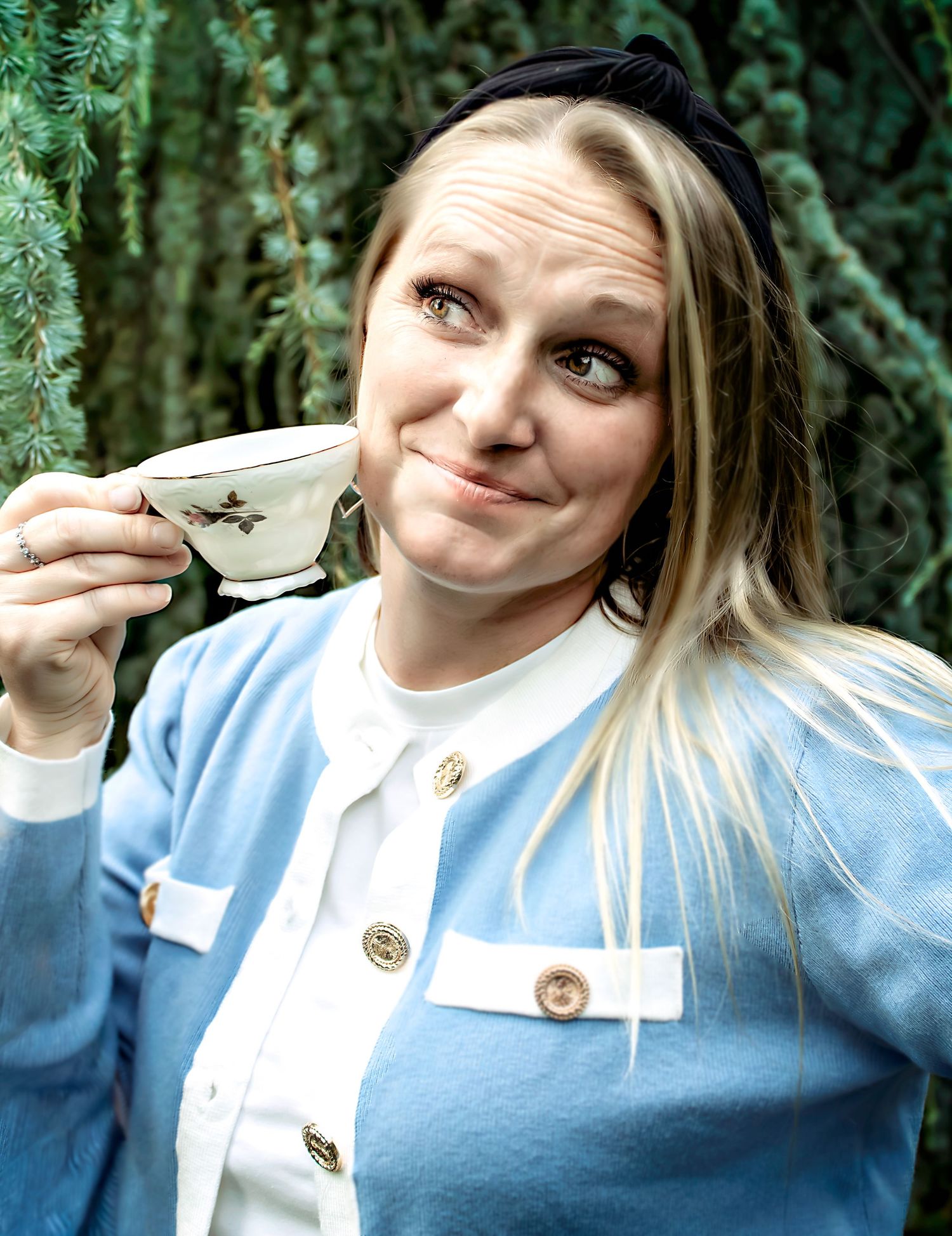 Someone in a light blue sweater makes playful expressions while holding a teacup.