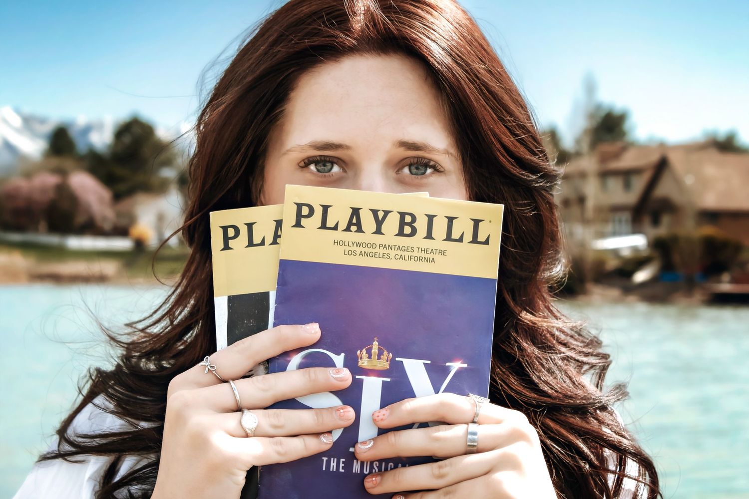 Person holding up Playbill program against scenic waterfront backdrop.