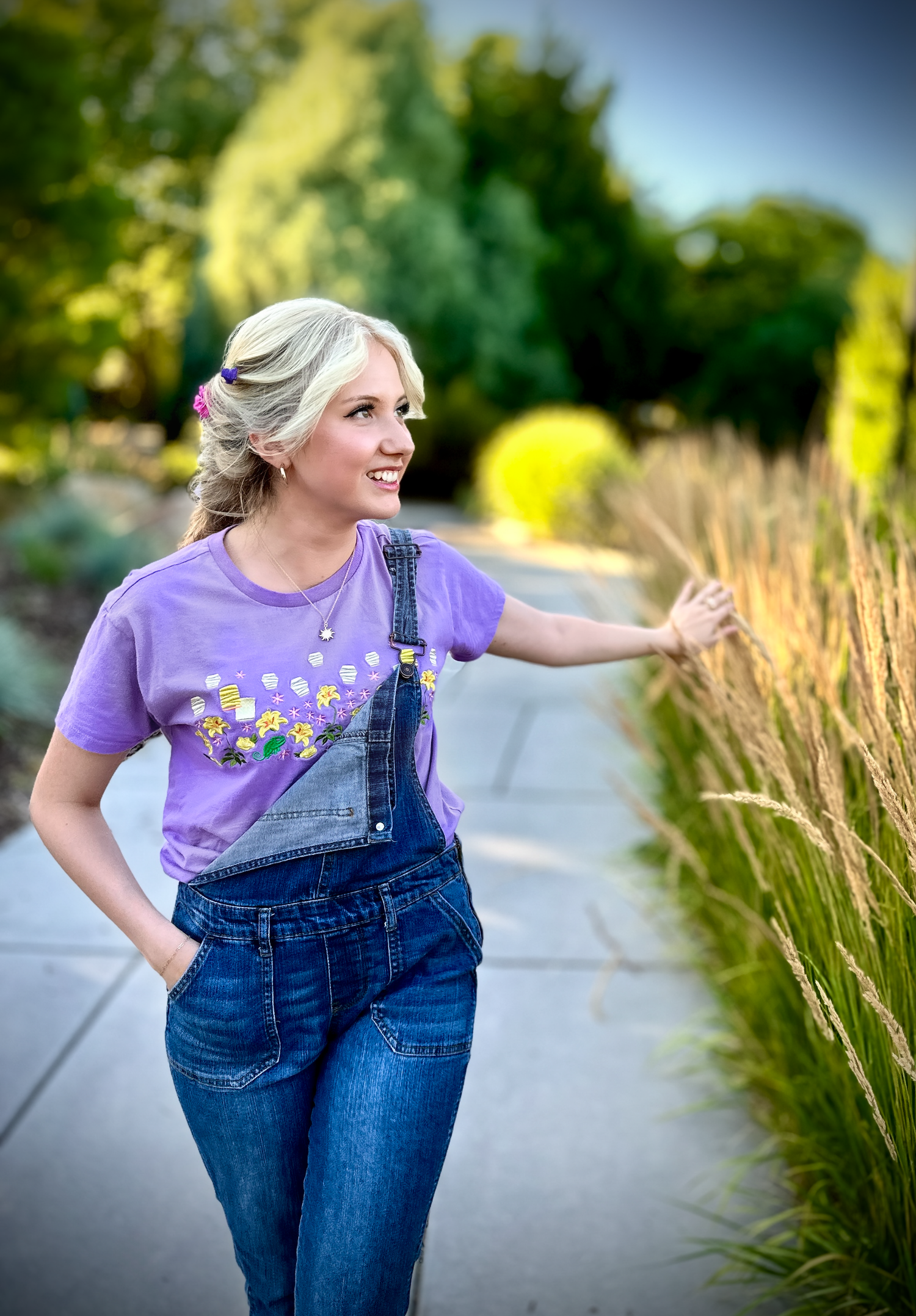 Figure in purple shirt and overalls walking joyfully along a path with ornamental grasses.