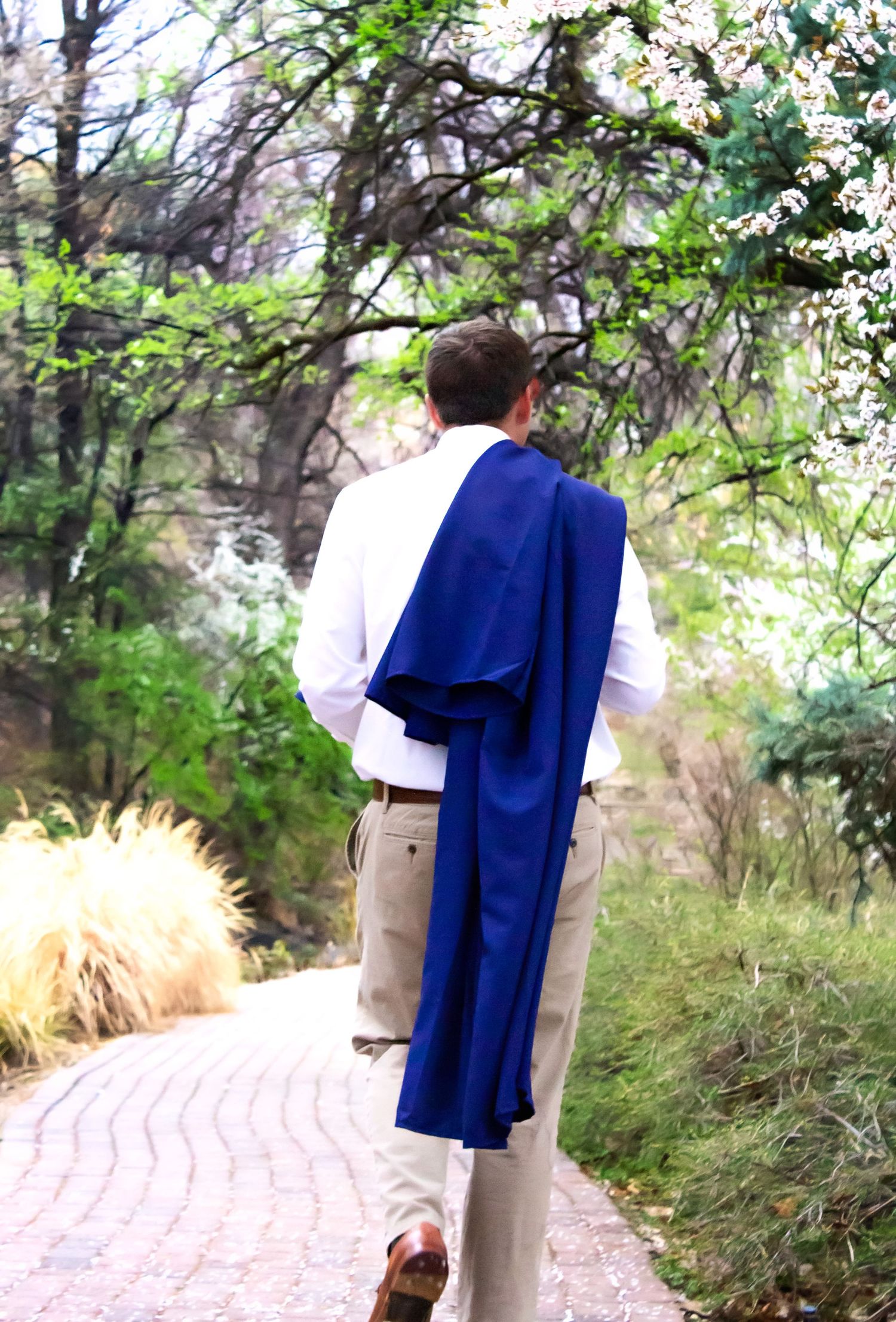 Graduate in formal attire and blue graduation gown walks along a winding garden path.