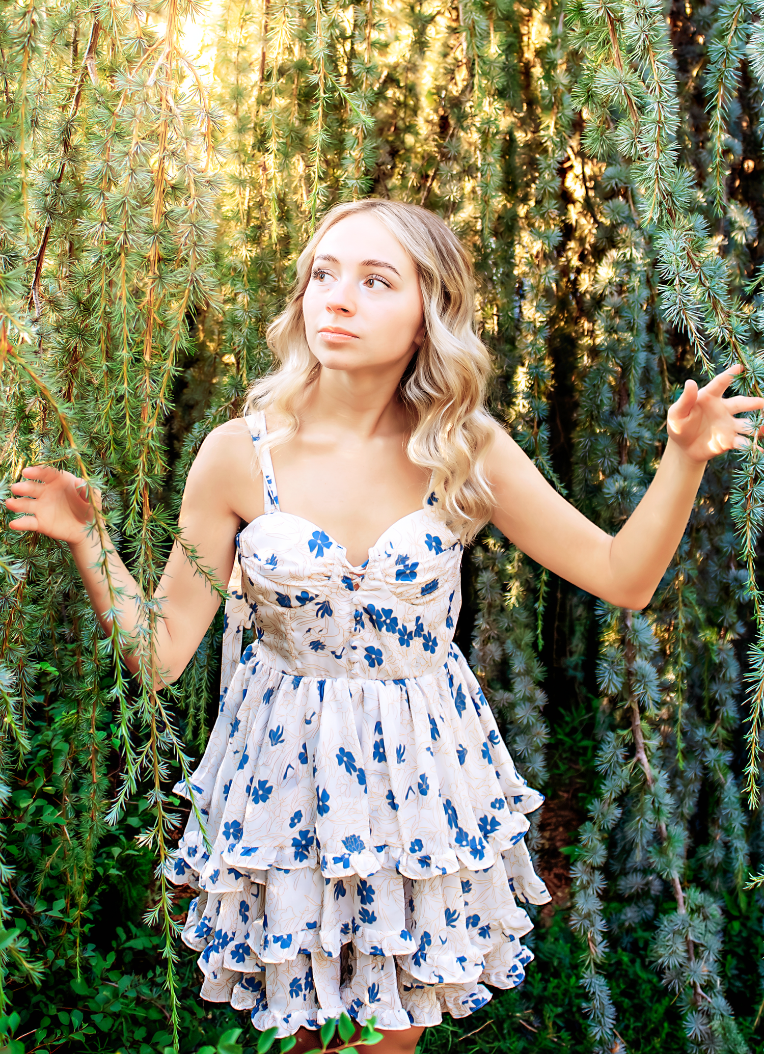 Playful poses captured in a garden setting wearing a ruffled blue and white floral dress.