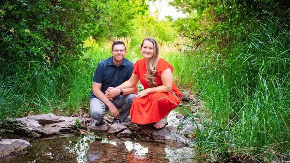 Couple sits together by a peaceful stream surrounded by lush green vegetation.