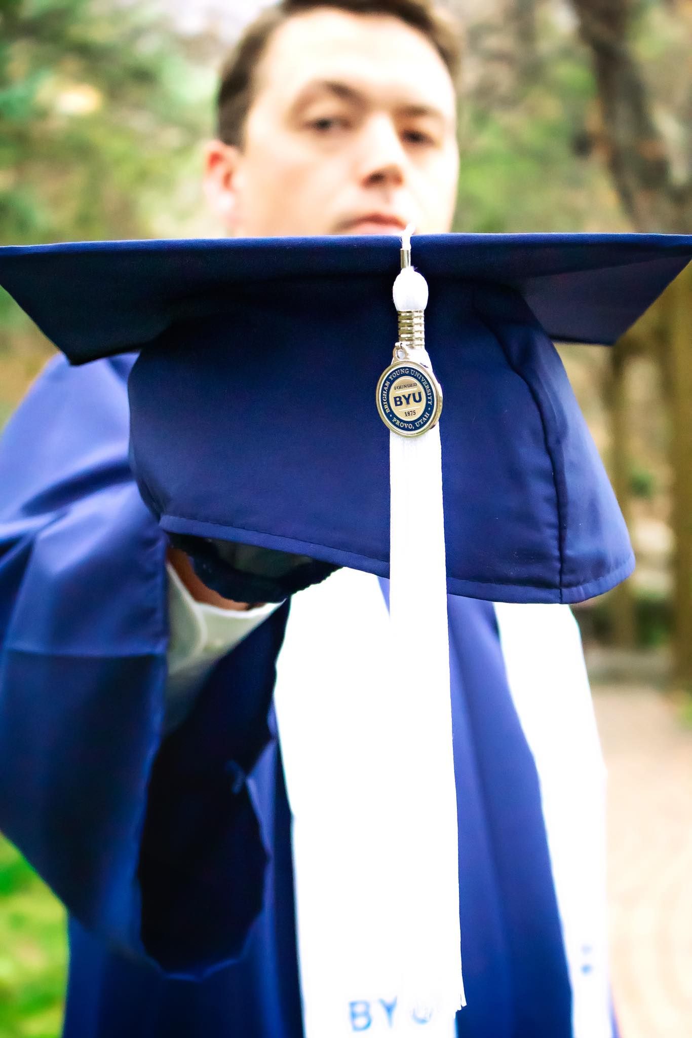 Close-up of a blue graduation cap with white tassel against a blurred natural background.