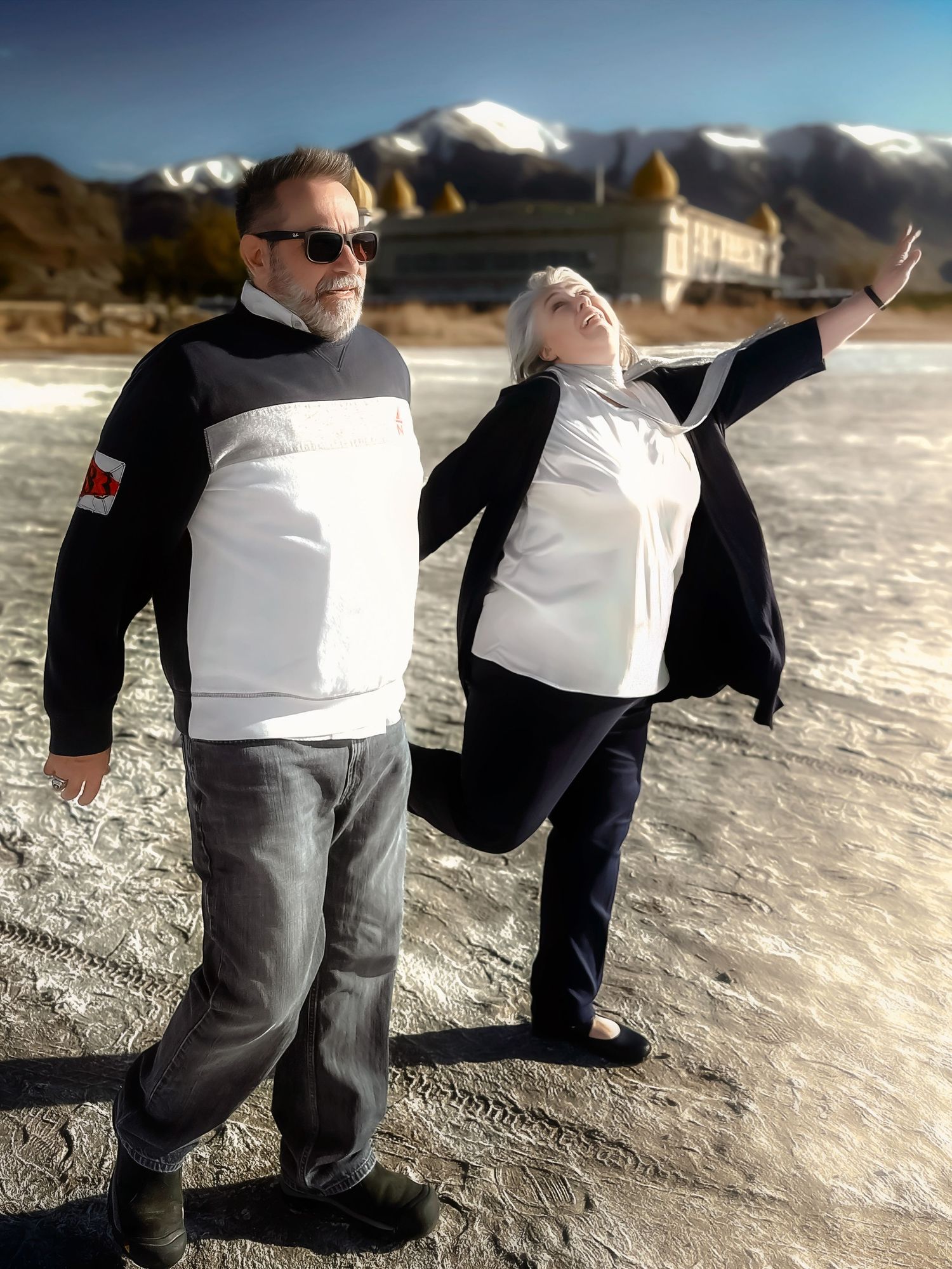 Playful couple embraces on a beach with snow-capped mountains in the background.