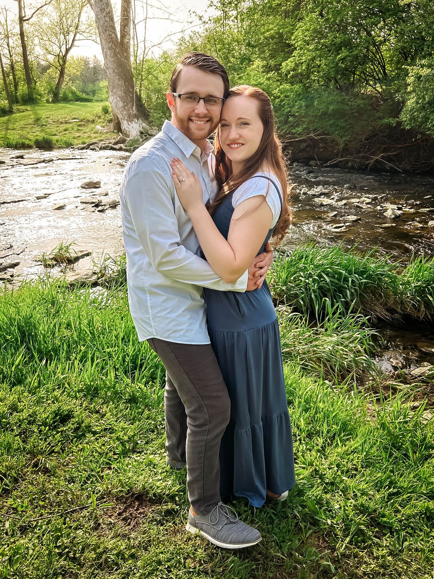 A romantic outdoor photoshoot by a stream with lush green grass and natural scenery.