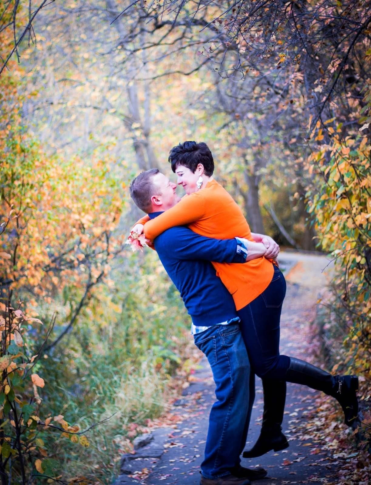 Couple sharing a romantic embrace on an autumn path surrounded by colorful fall foliage.