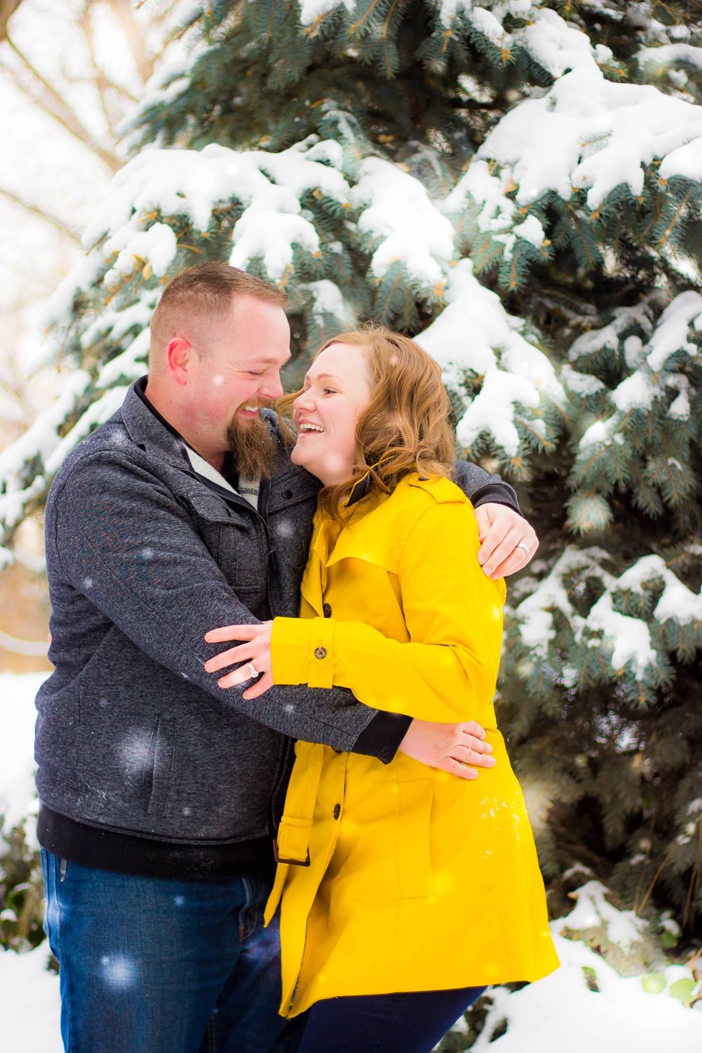 Couple sharing intimate moment in winter scene with snow-covered evergreens.