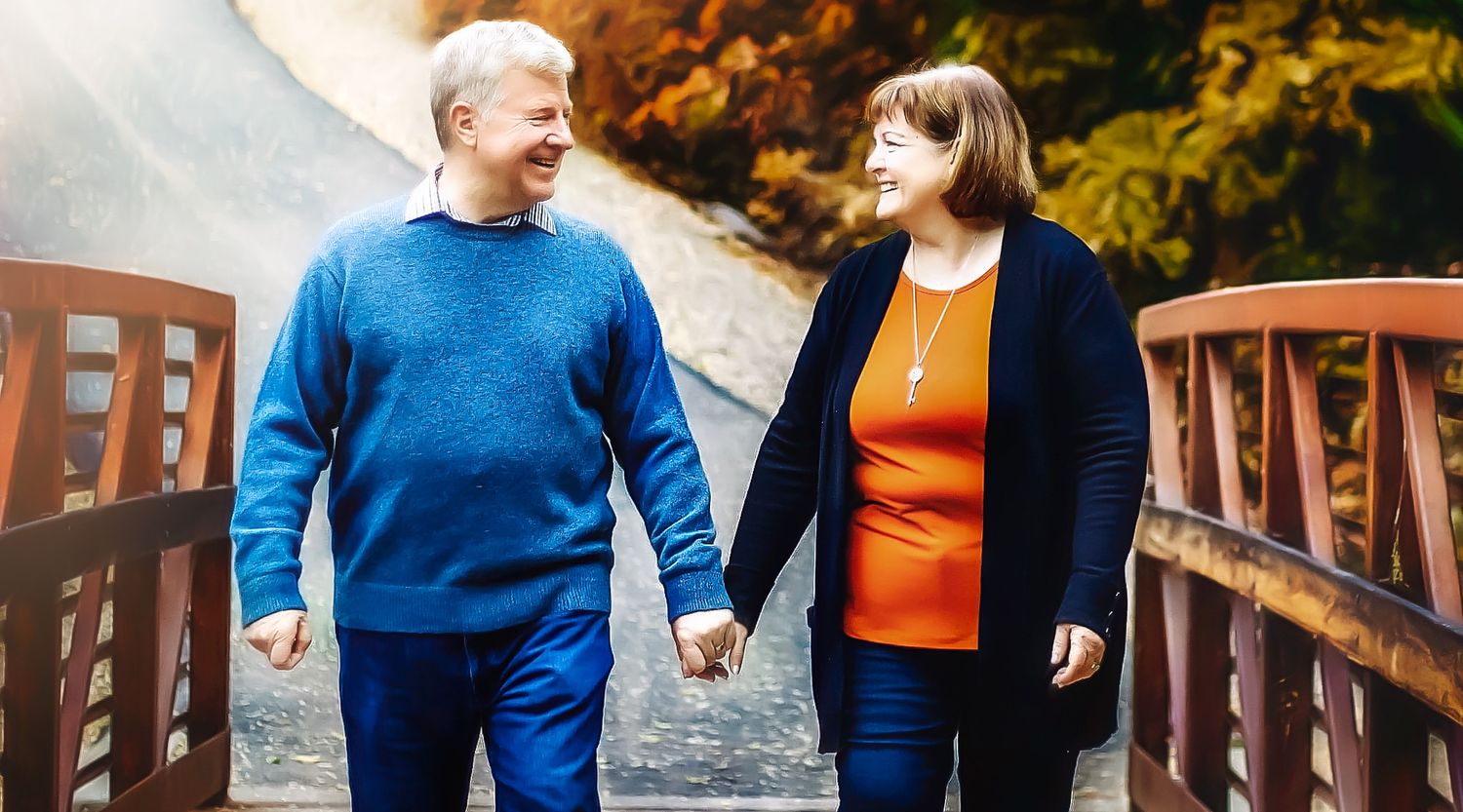 A couple strolls together on a path with golden fall foliage in the background.