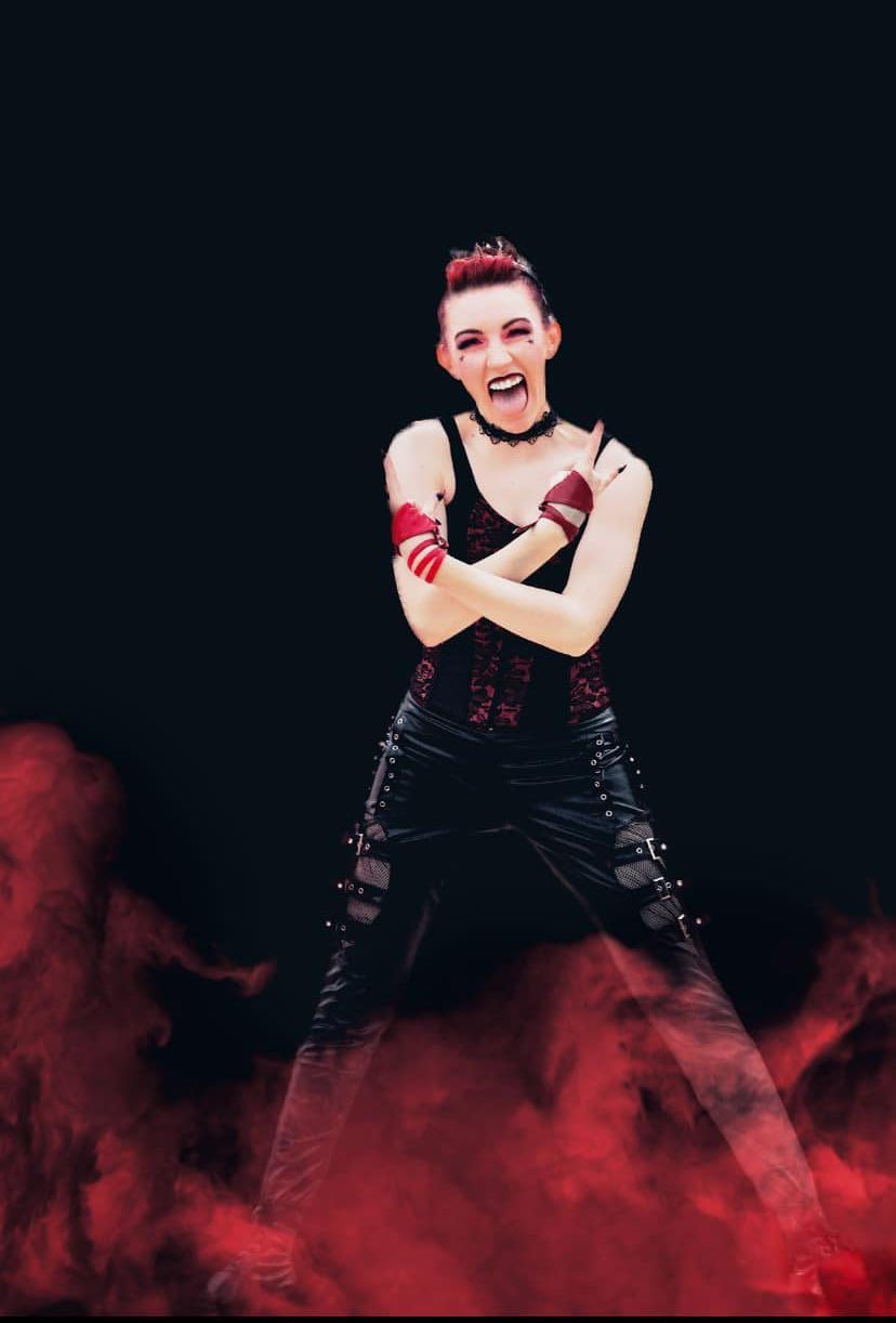 Energetic performer in black costume poses dramatically with red smoke effects.