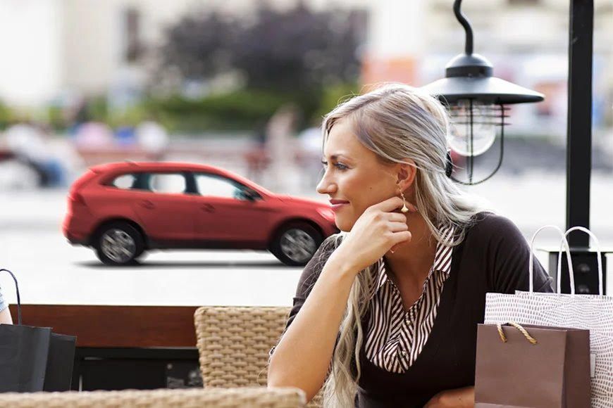 Person seated at outdoor cafe with street view and parked cars visible in background.