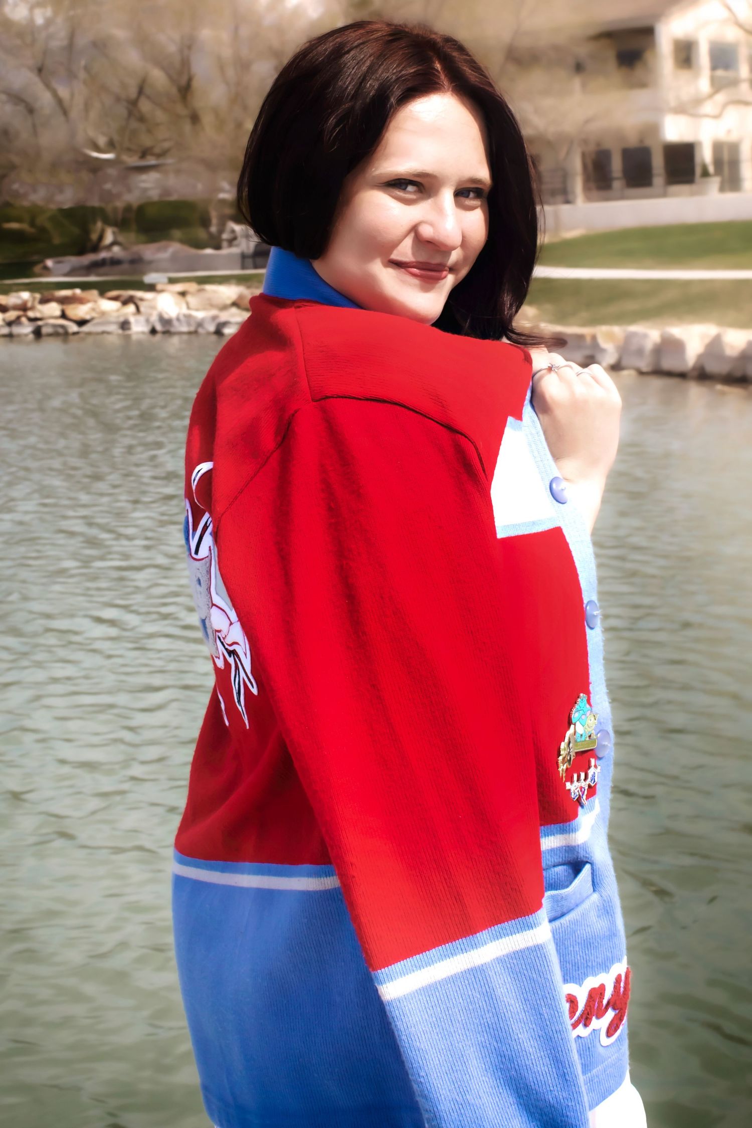 Person wearing red and blue athletic jacket poses by lakeside.