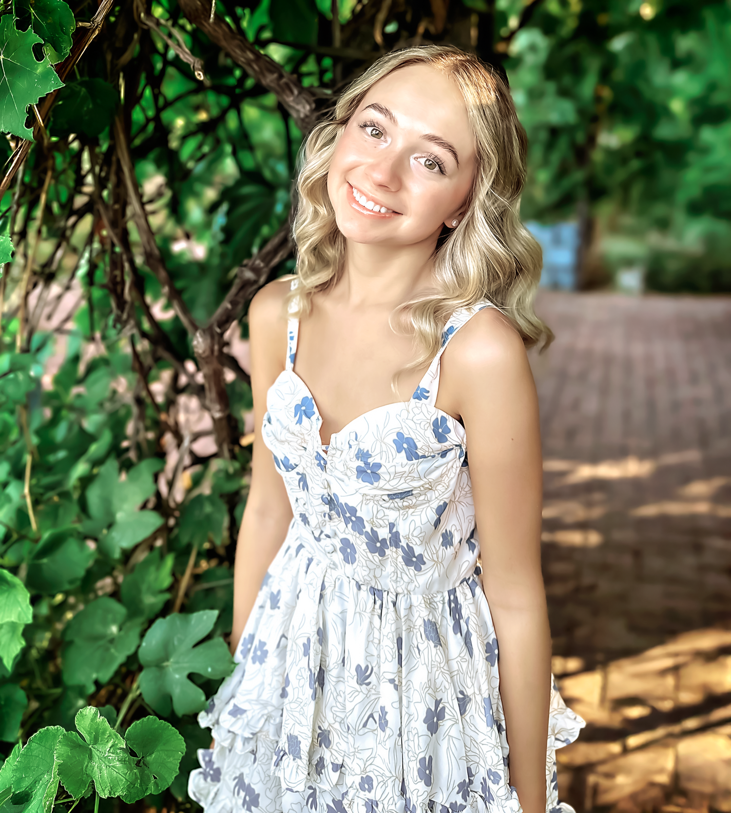 Outdoor photoshoot featuring a blue and white floral dress among green foliage.