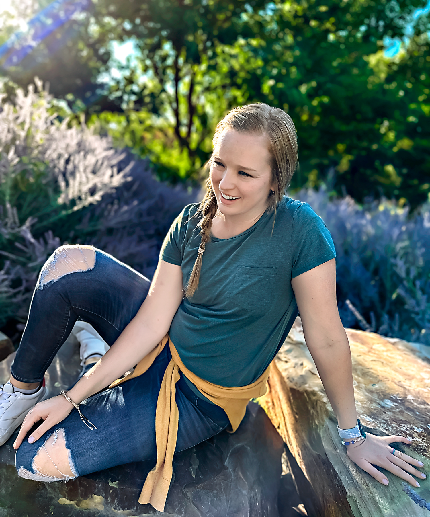 Person wearing navy shirt and yellow scarf sits casually on outdoor rocks.