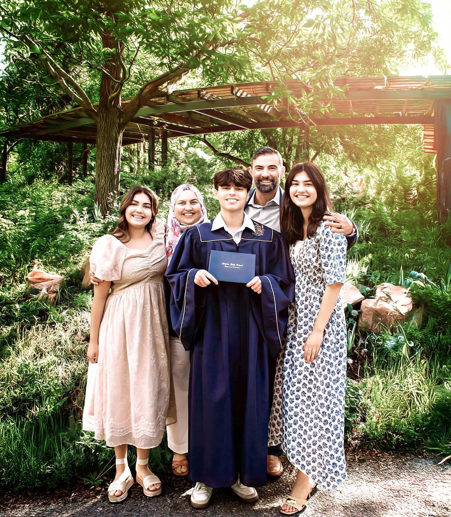 Children in graduation caps and dresses pose together in garden setting.