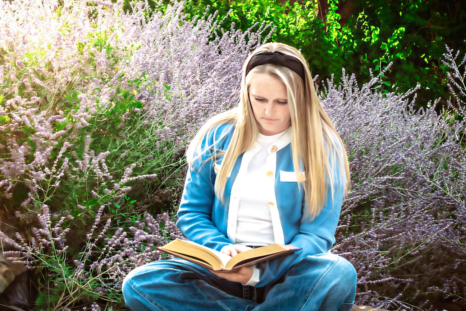 Person reading outdoors surrounded by lavender and greenery in dappled sunlight.
