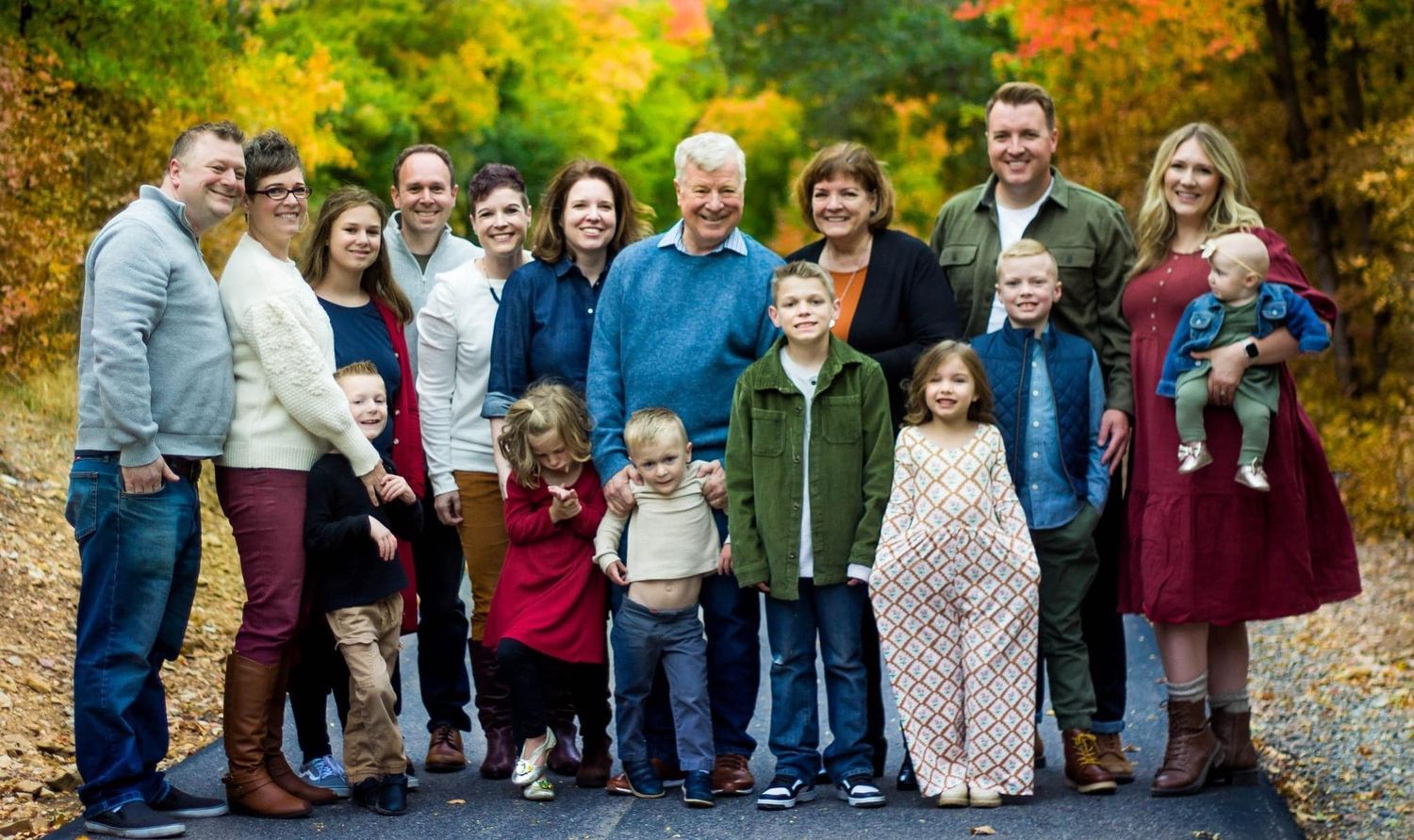 Large family group portrait taken outdoors during autumn with colorful fall foliage.