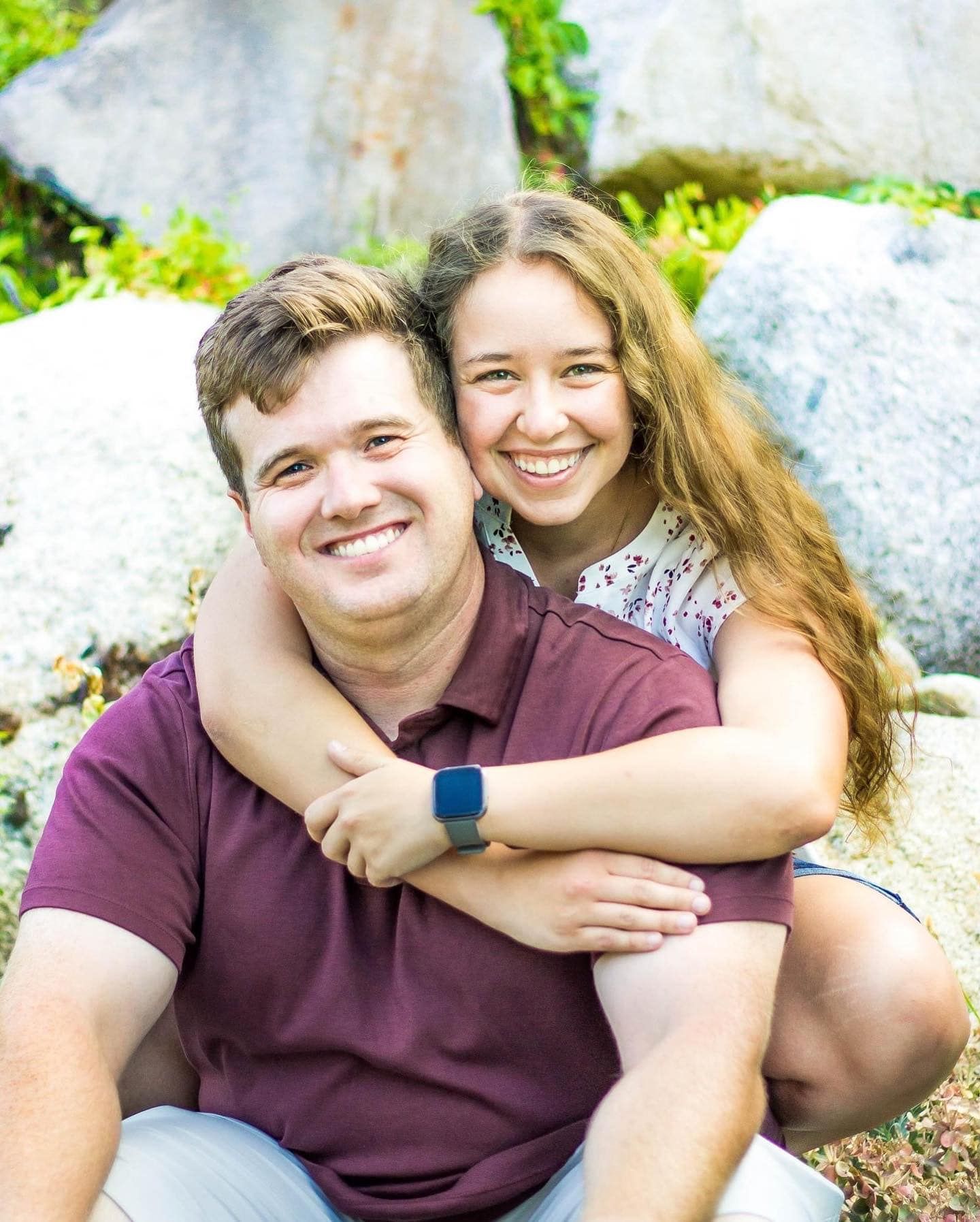 Couple sharing joyful moment while sitting on rocks with natural backdrop.