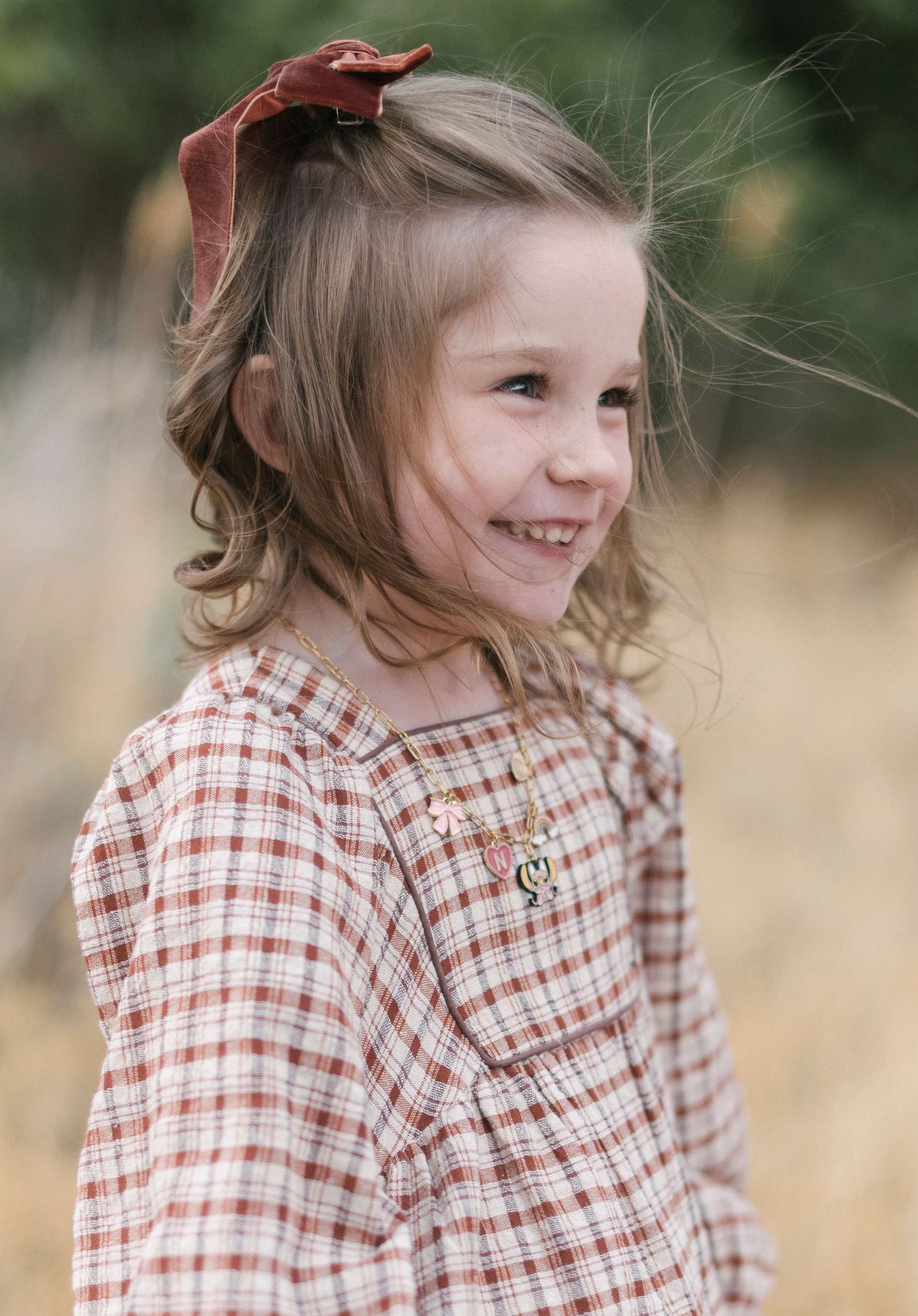 Young girl in plaid shirt smiling and looking to the side in natural setting.