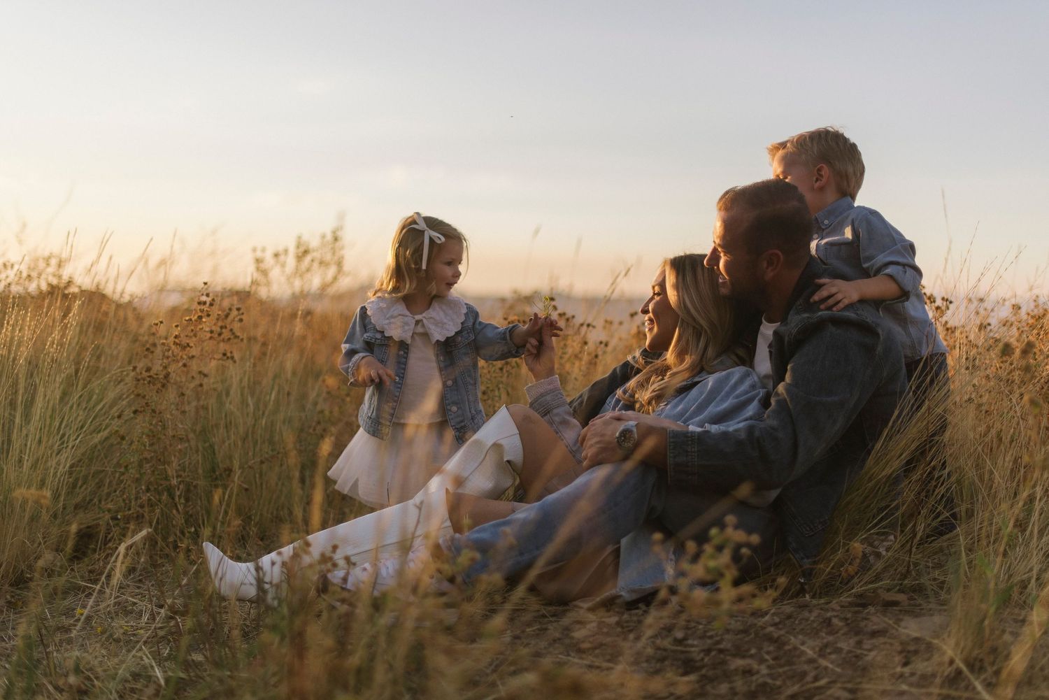 Family relaxing together in tall grass during sunset golden hour.
