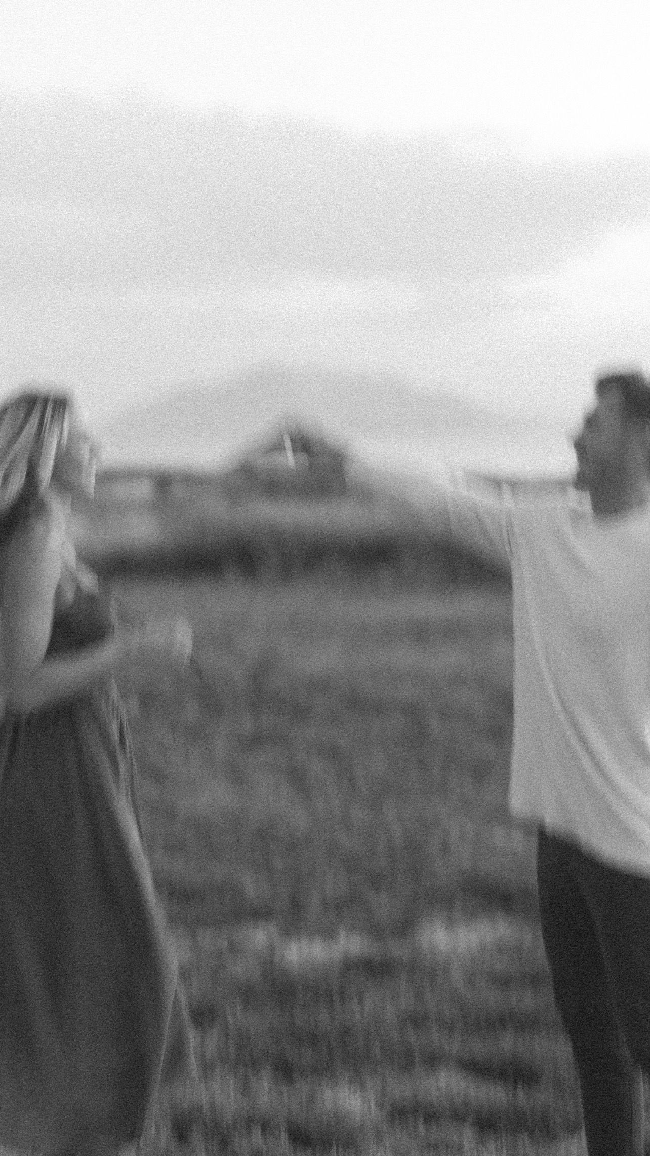 Black and white silhouette of two people in field with mountains in background.