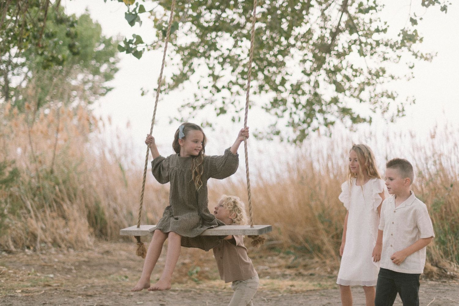 Children playing on a wooden swing in a natural outdoor setting.