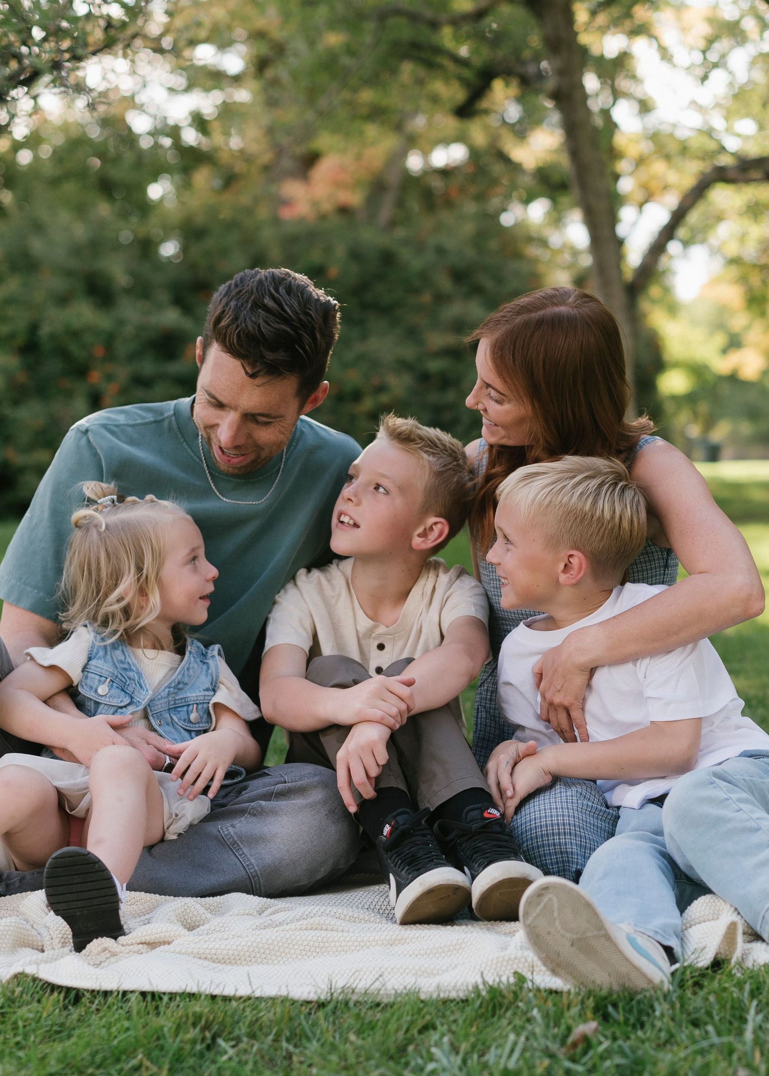 Family lying together on blanket in grass having intimate conversation.