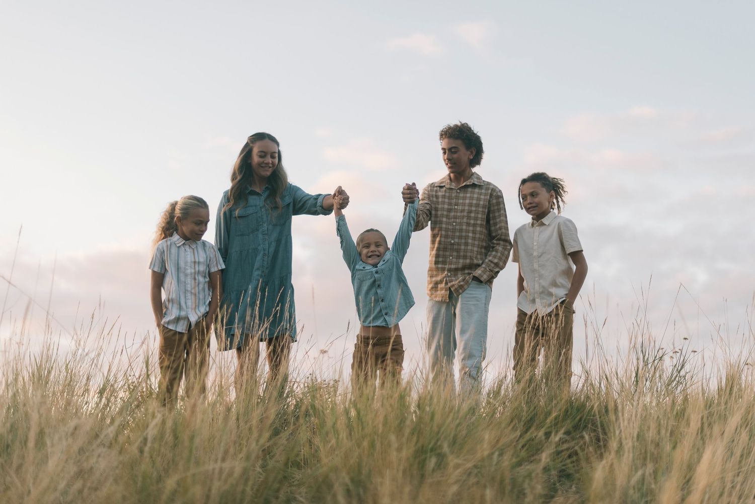 A family stands together in tall grass against a cloudy sky during sunset.