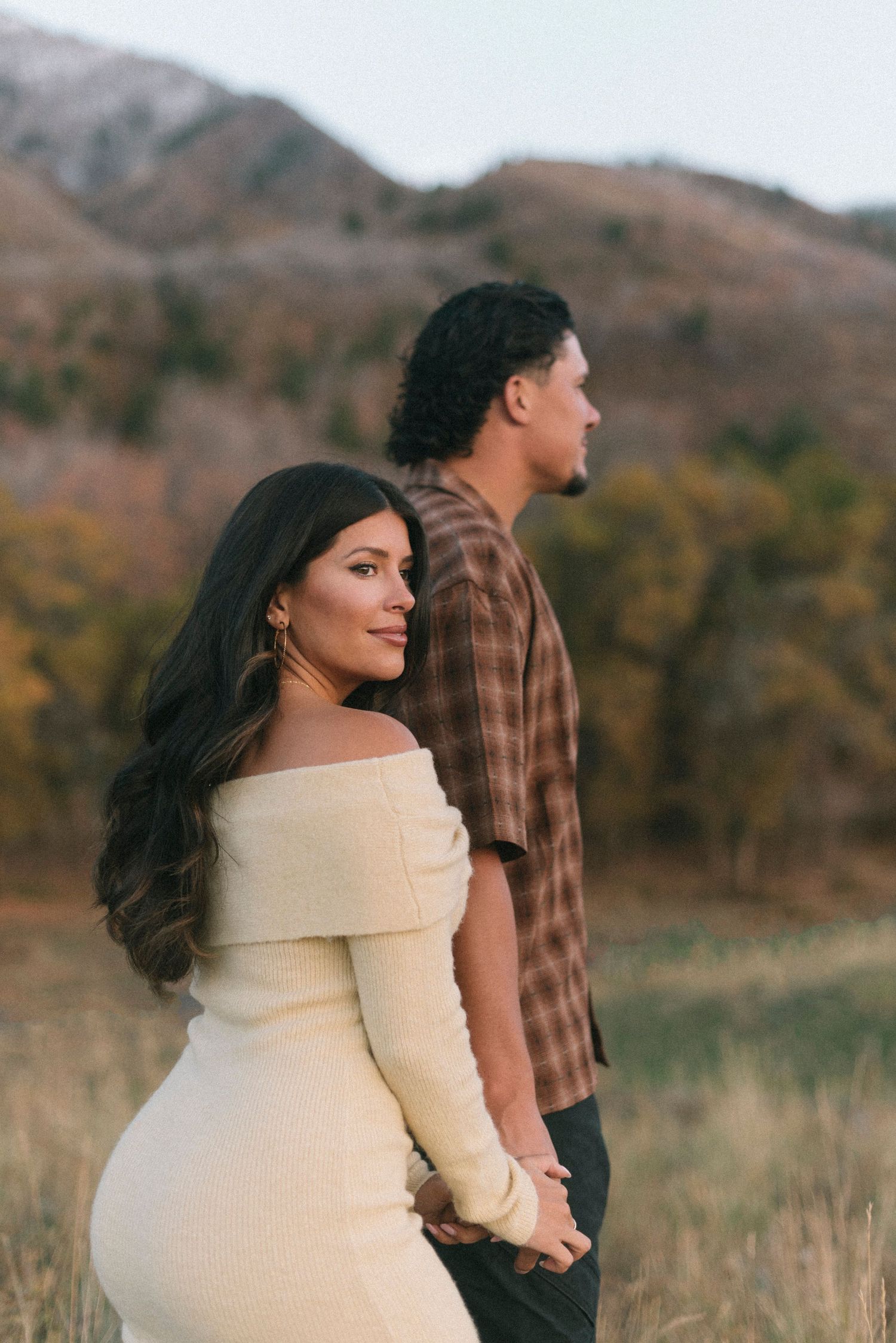 A couple poses in a mountain meadow during an autumn photoshoot.
