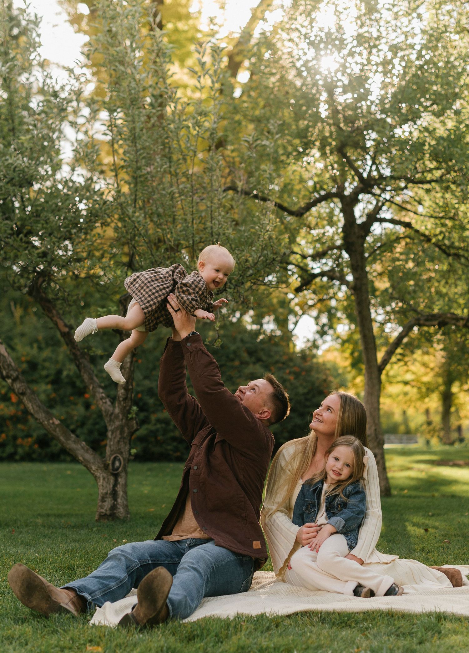 Family lying on grass having fun together in an orchard during golden hour.