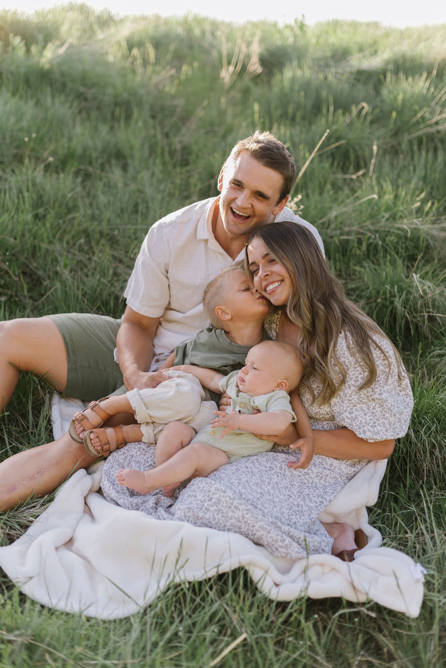 A family relaxing together on a blanket in tall grass during golden hour.