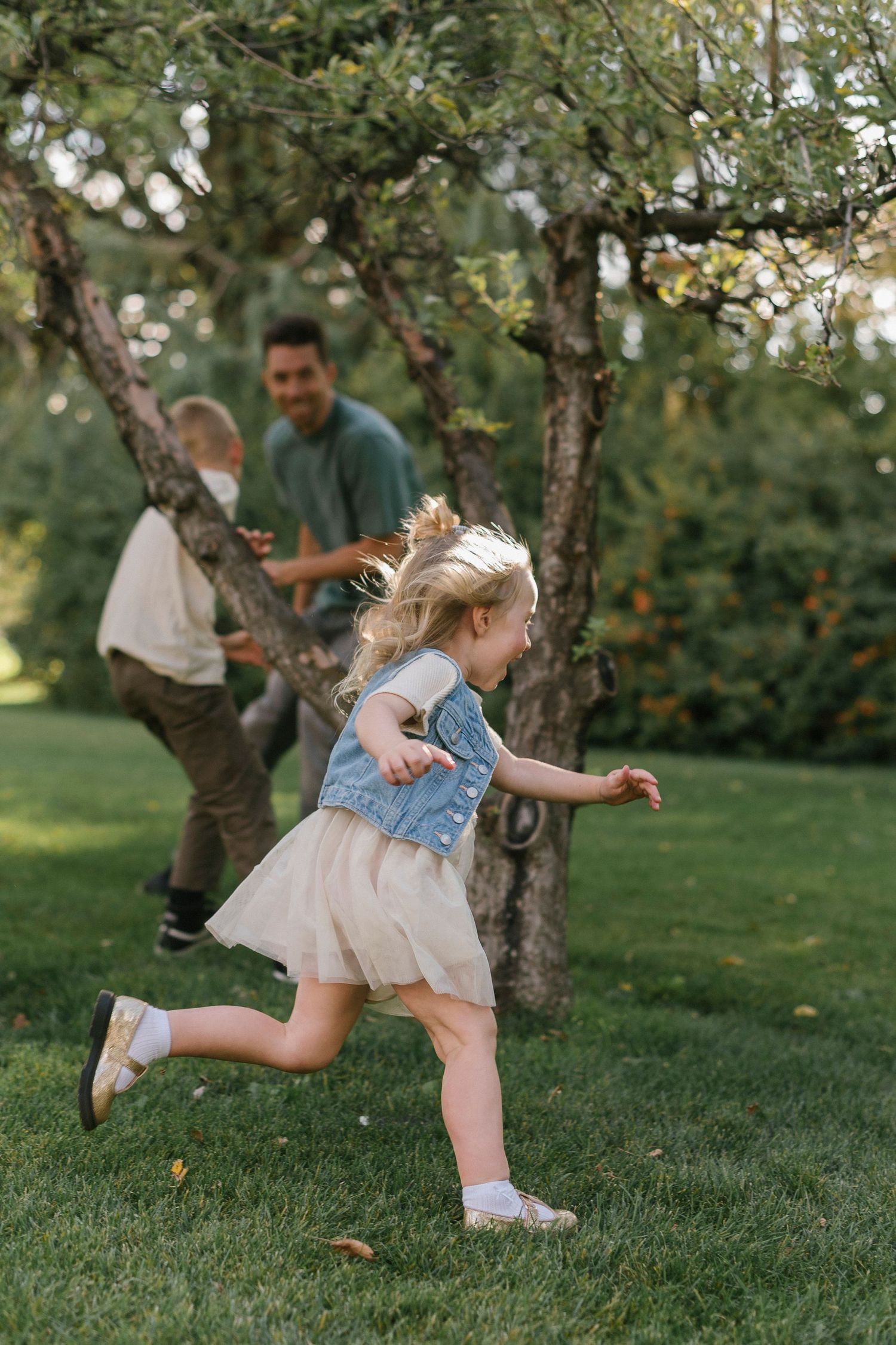 A series of playful action shots showing a child in a tulle dress and denim vest jumping and twirling in a garden setting.