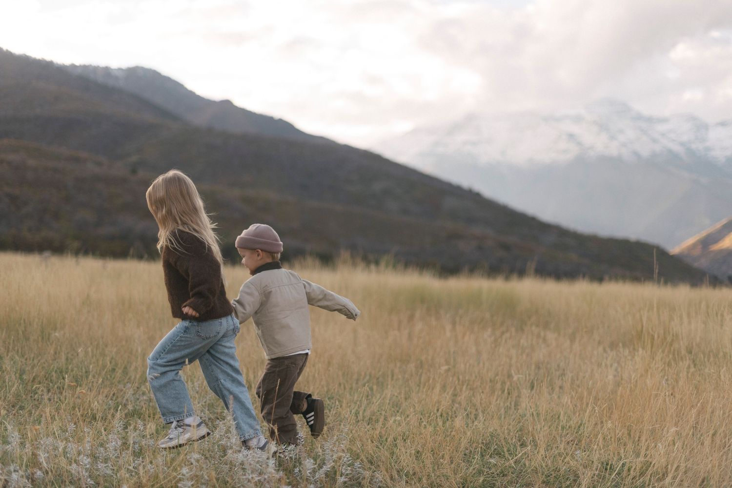 Family walking together through a golden field with mountains in the background at sunset.