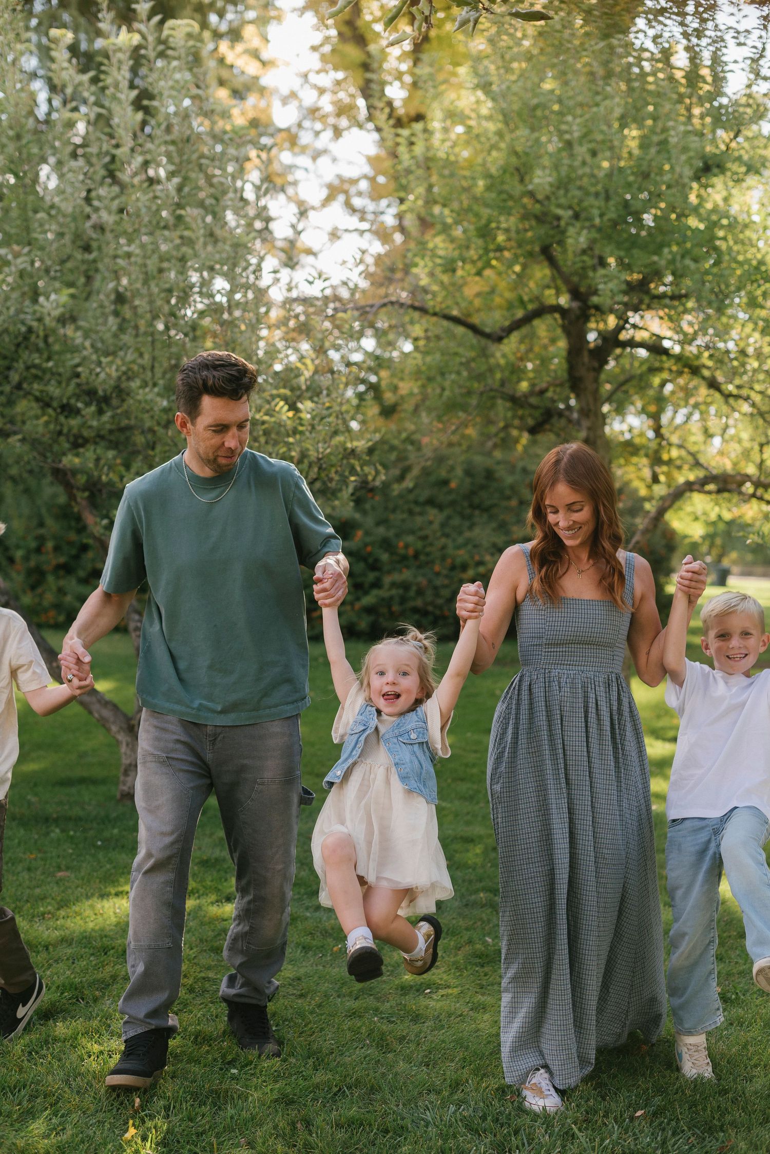 Family playing and swinging children while walking through green grass.