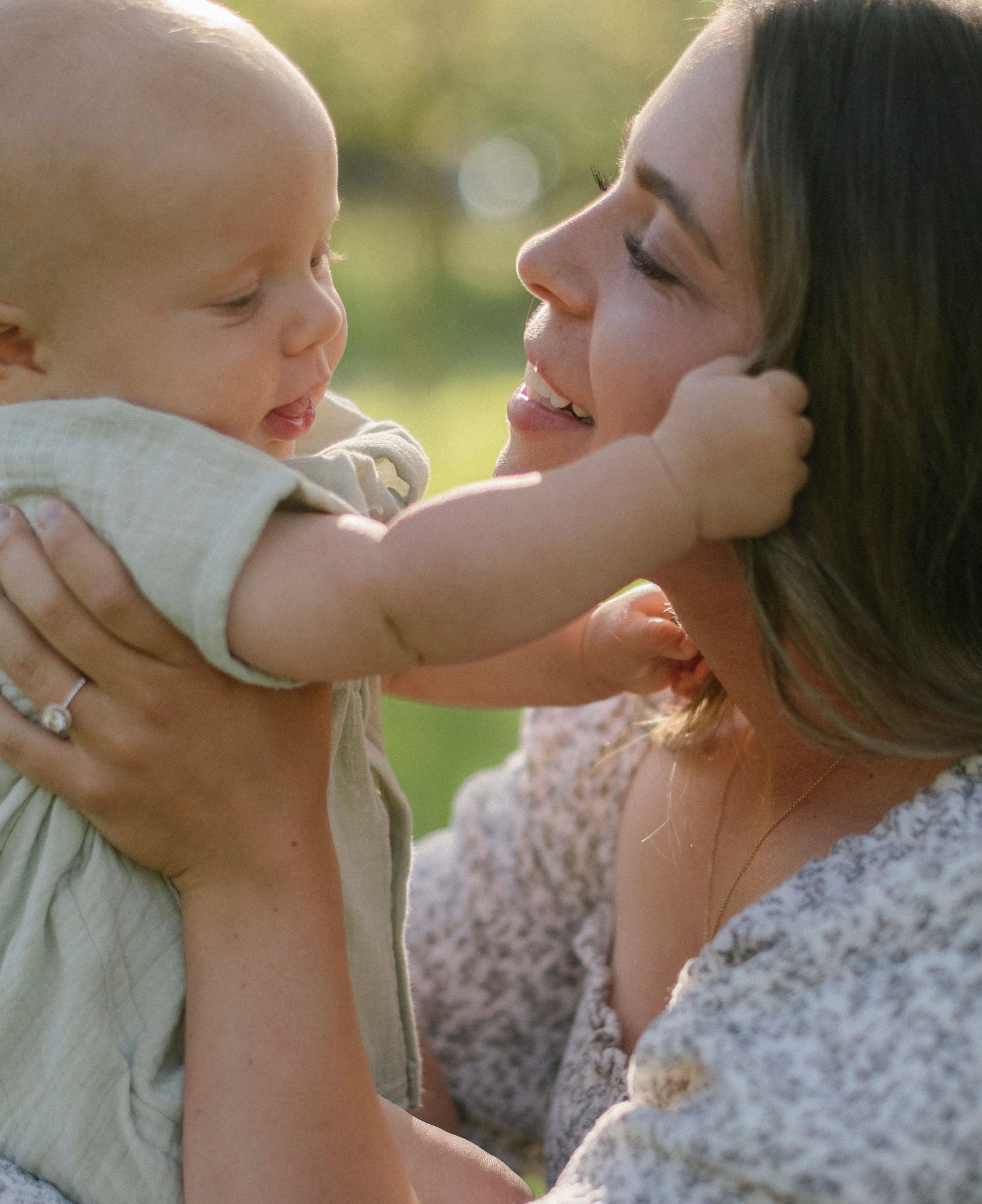 A tender moment captured between a baby and adult in sunlit outdoor setting.