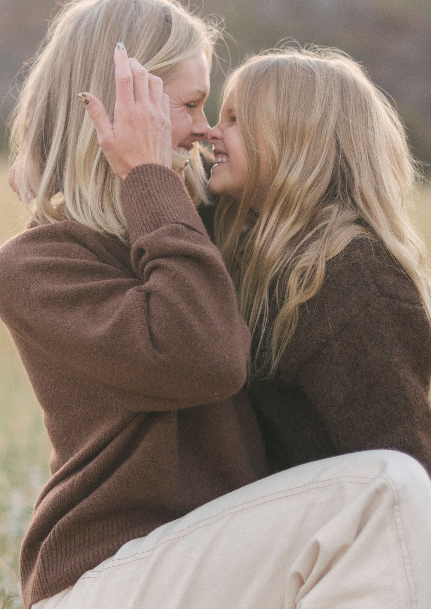 Two people sharing an intimate moment in brown sweaters against a mountain backdrop.