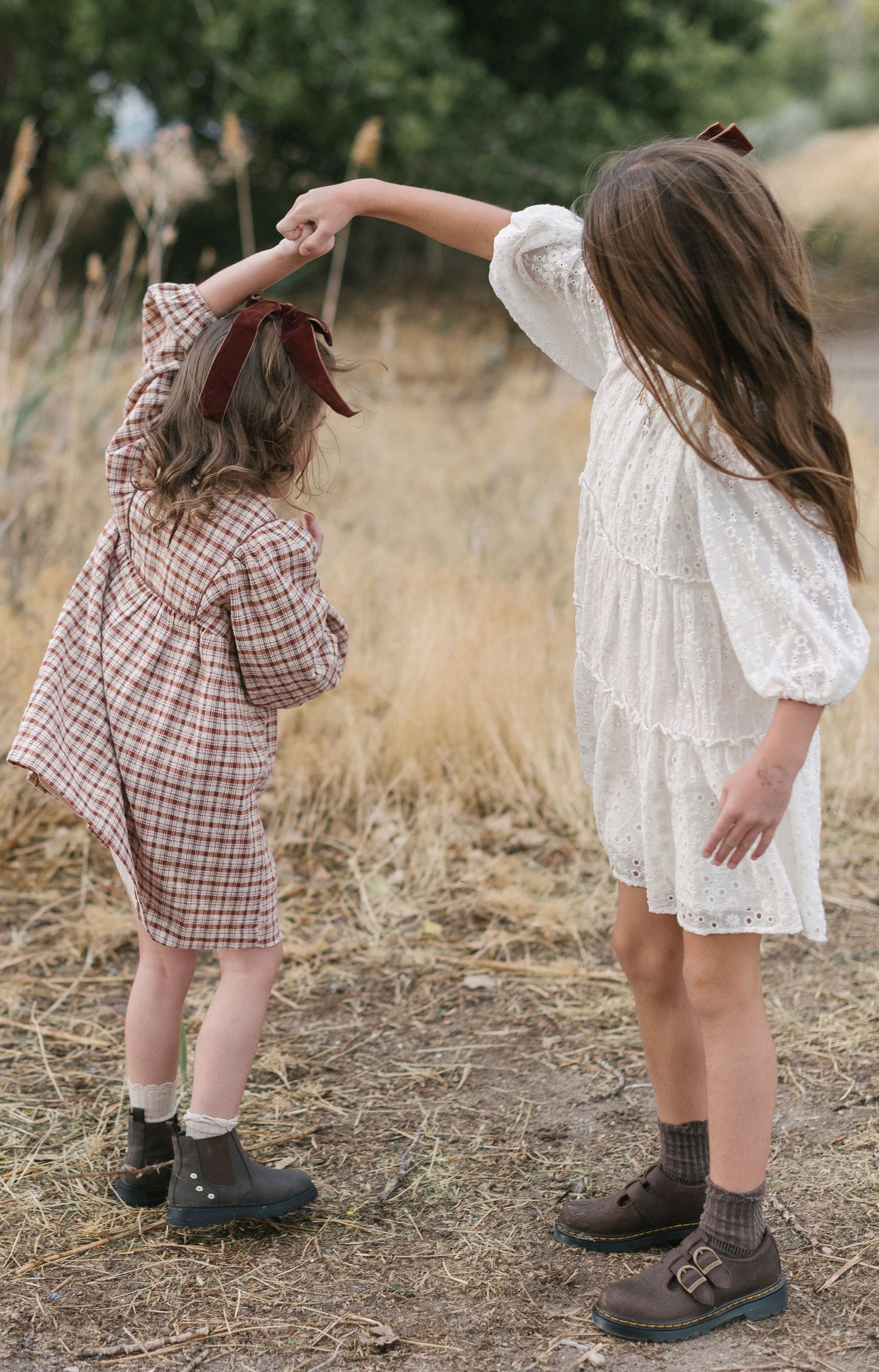 Close-up shots of children's feet wearing boots on dry grass in alternating white dress and plaid outfits.
