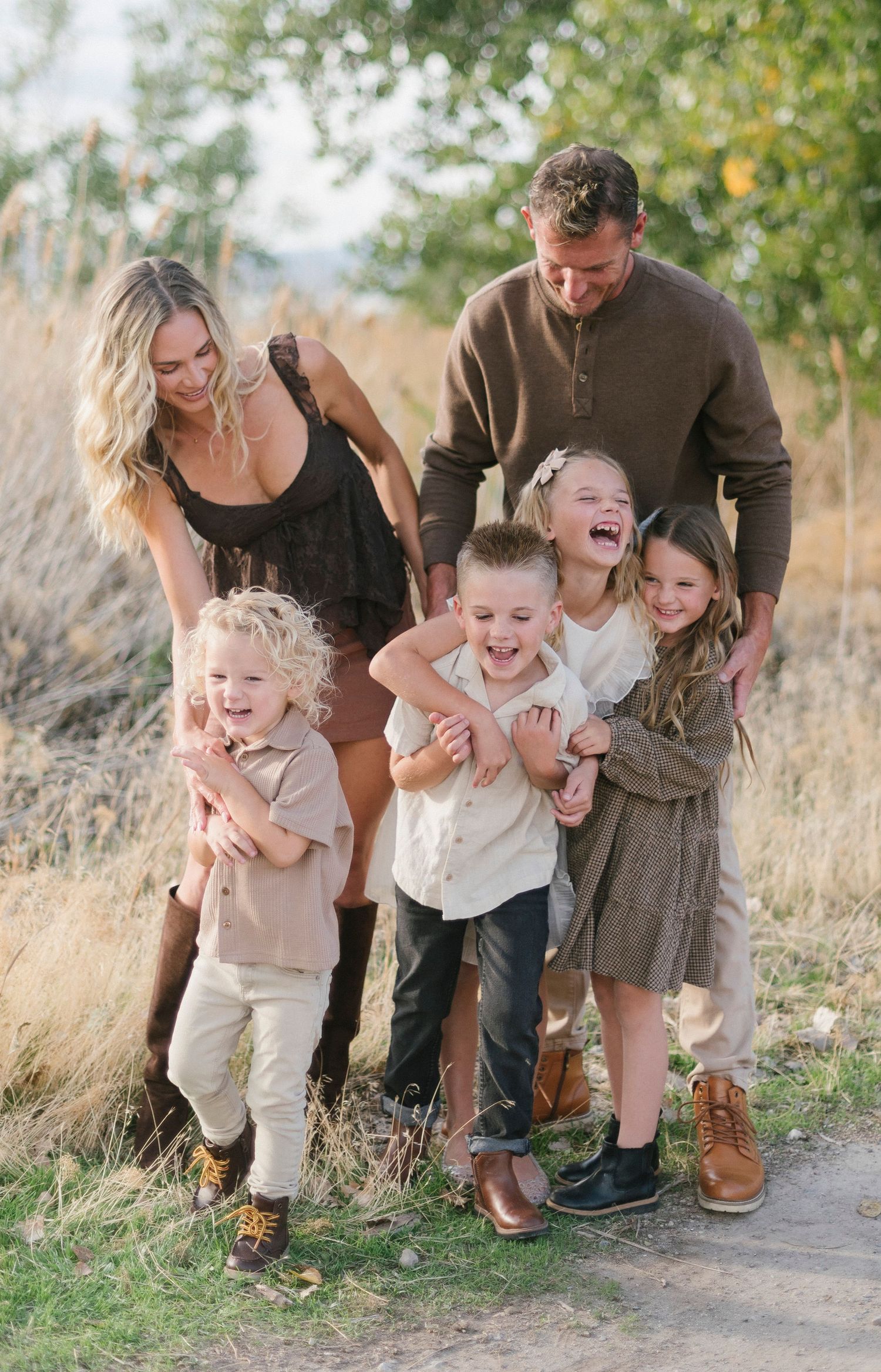 A playful family moment captured in tall grass with everyone laughing together.