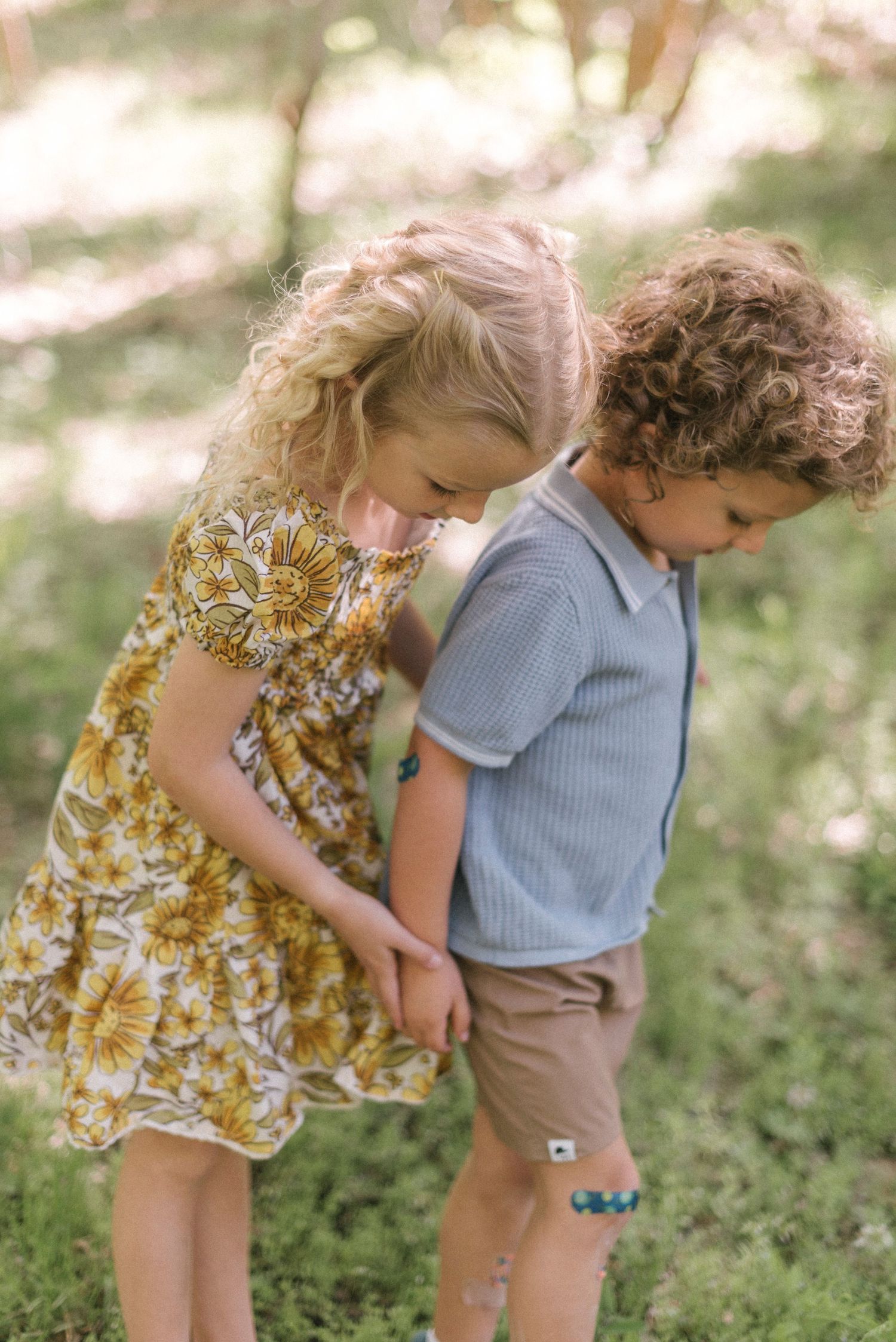 Two young children in floral and blue outfits examining something interesting on the ground.