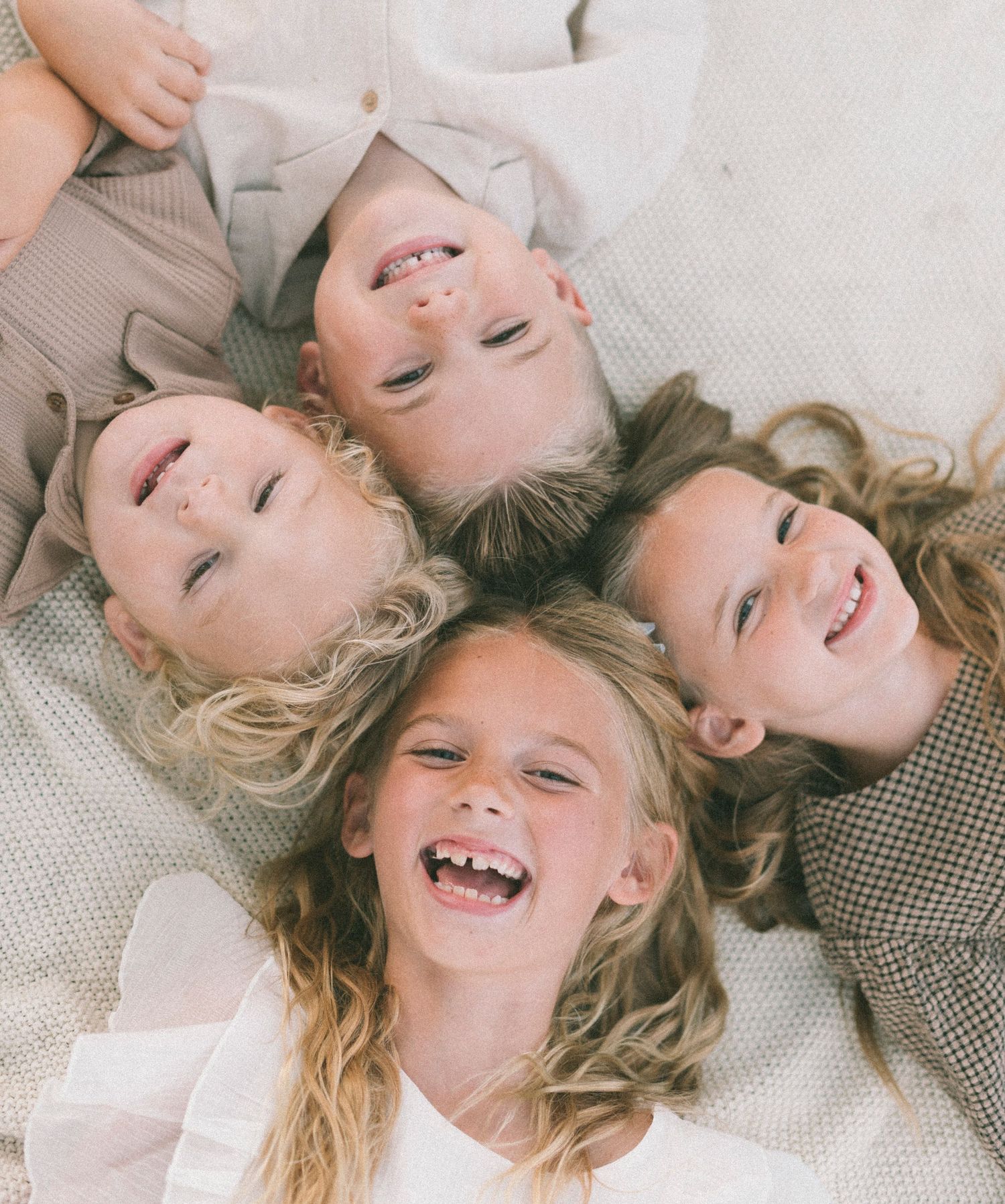 Children lying in a circle on a blanket with their heads together, laughing and smiling.