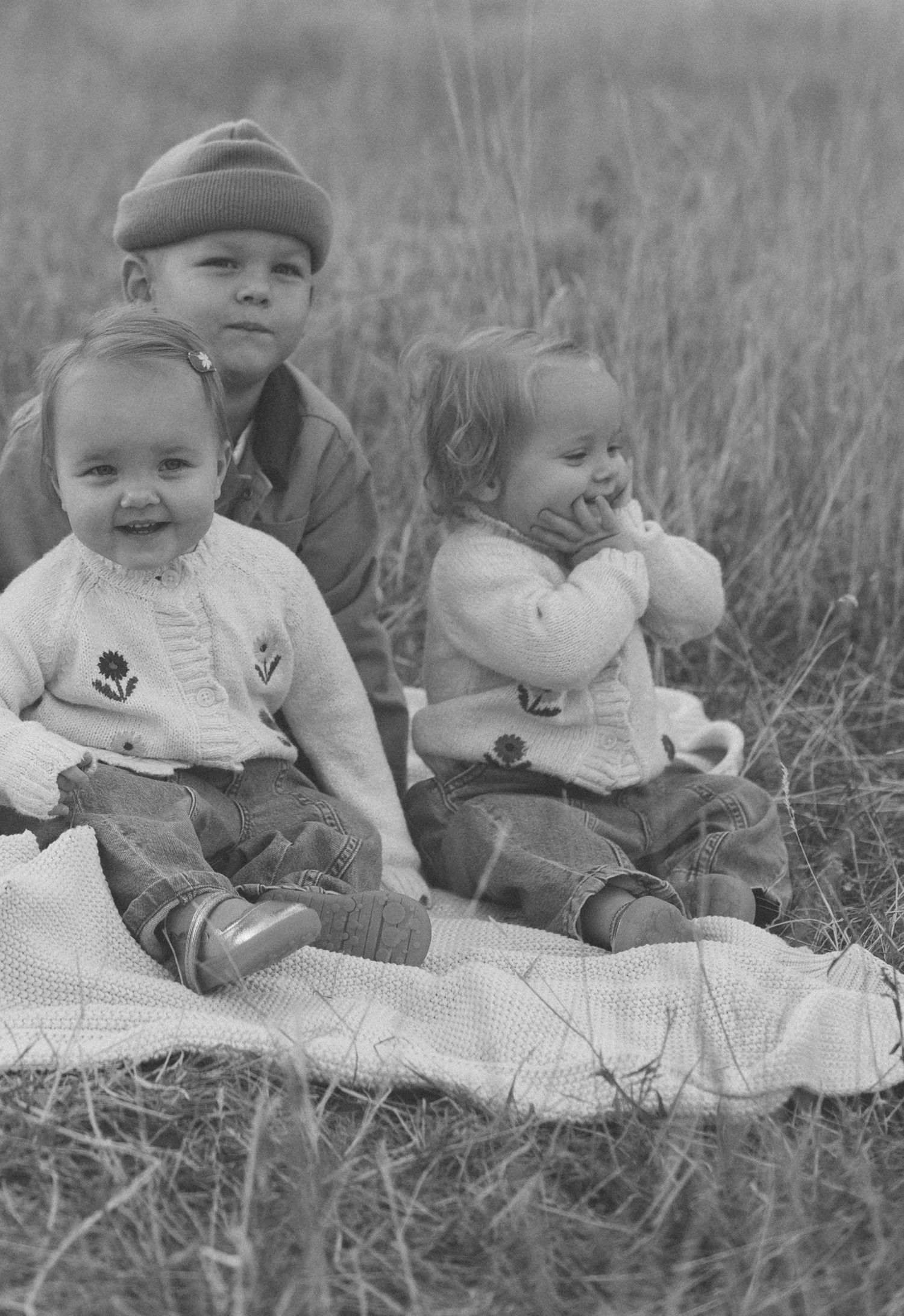 Vintage black and white photograph of children sitting together on a blanket outdoors.
