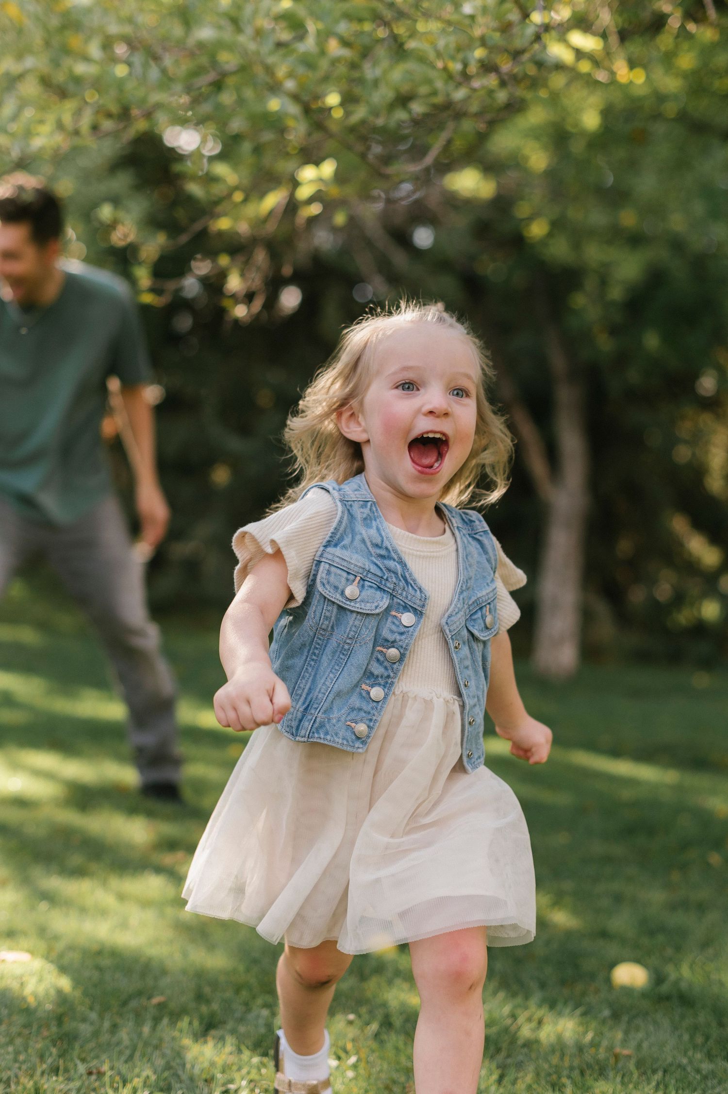 A sequence of joyful moments capturing a young child running and laughing in a white dress and denim vest outdoors.