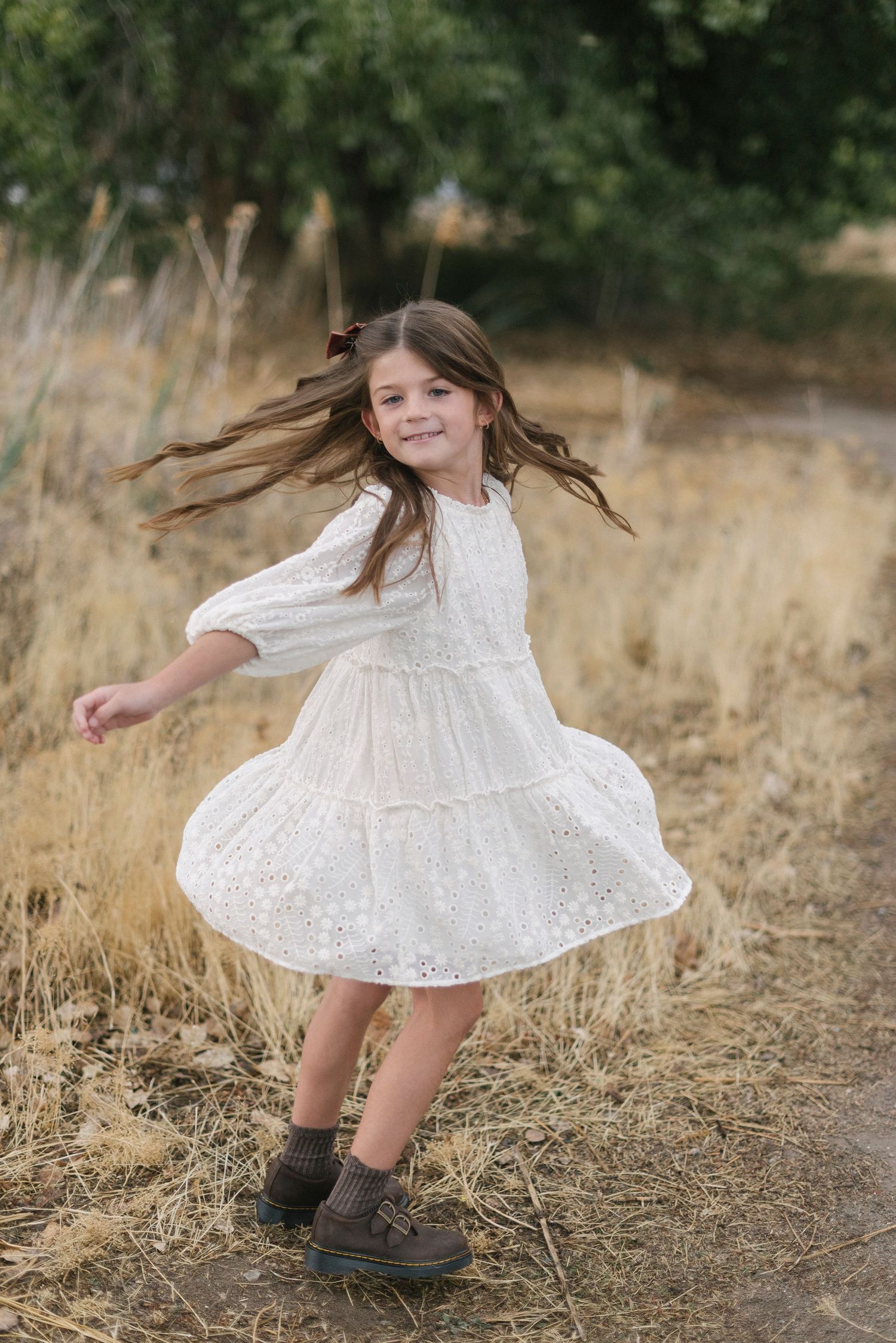 Young girl in white lace dress twirling and dancing in golden field.