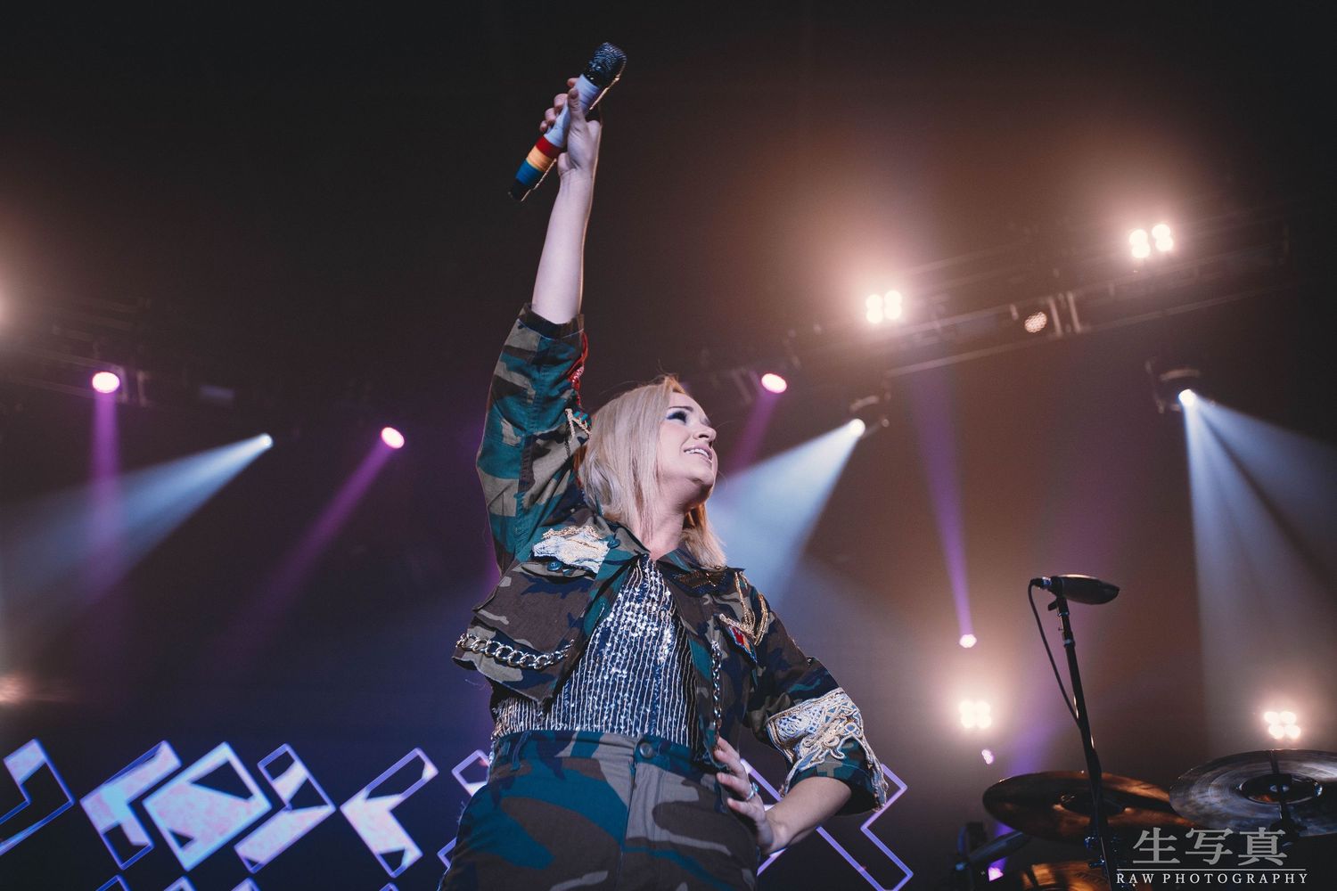 Energetic concert performer with raised arm on stage with dramatic purple lighting effects.