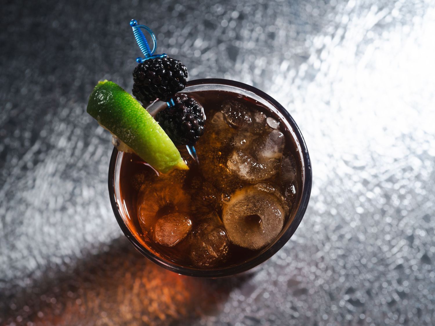 Dark cocktail with blue straw and celery garnish in moody lighting.